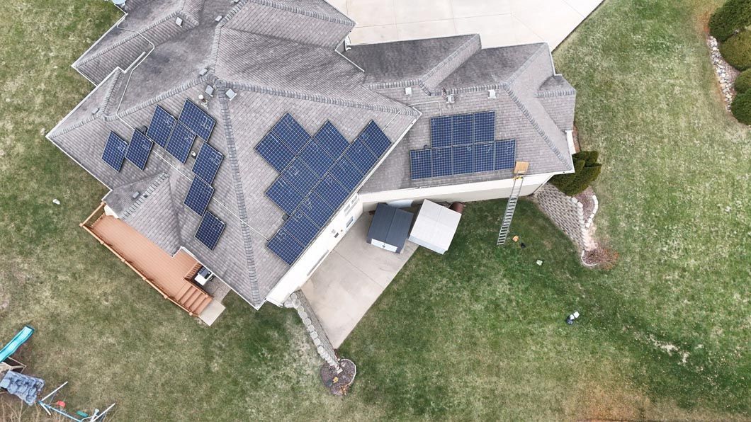 Aerial view of a house with solar panels on the roof, surrounded by green grass.