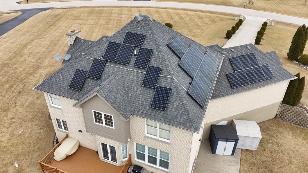 Solar panels on a two-story house with a tan exterior, set in a brown field.