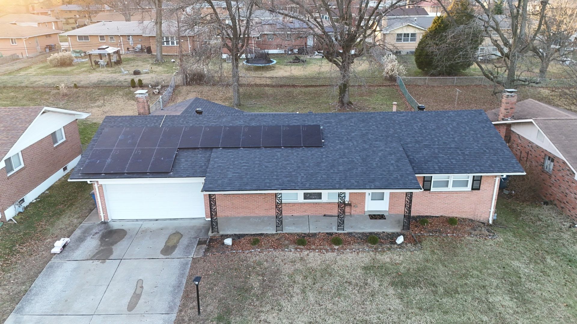 A house with solar panels on the roof, brick exterior, a driveway, and a porch in a residential area.