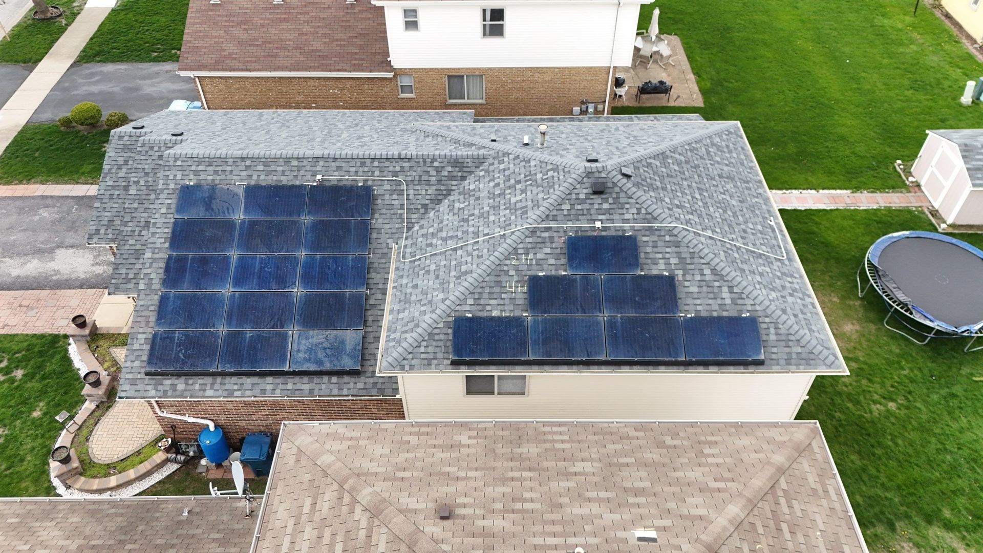 Overhead view of house with solar panels on a gray roof. Green grass and other homes are visible.