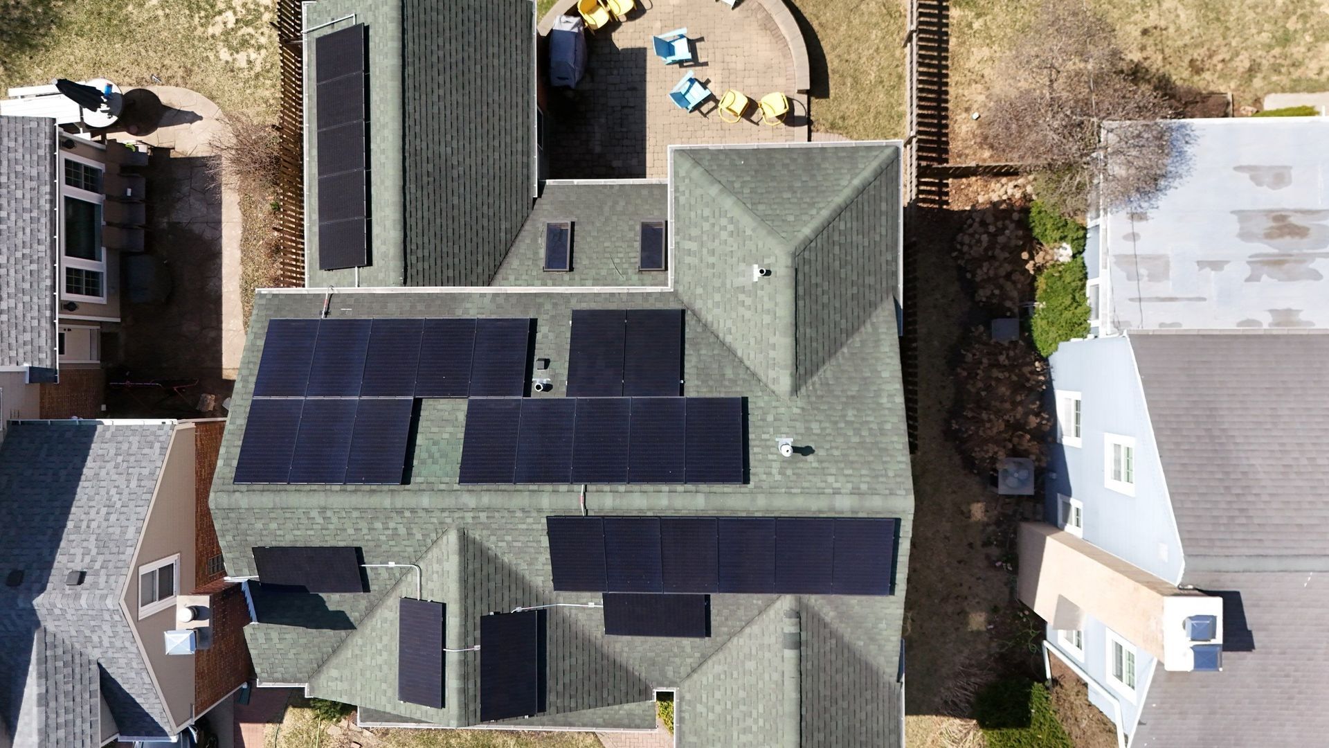 Overhead view of a house with solar panels installed on its green shingled roof.