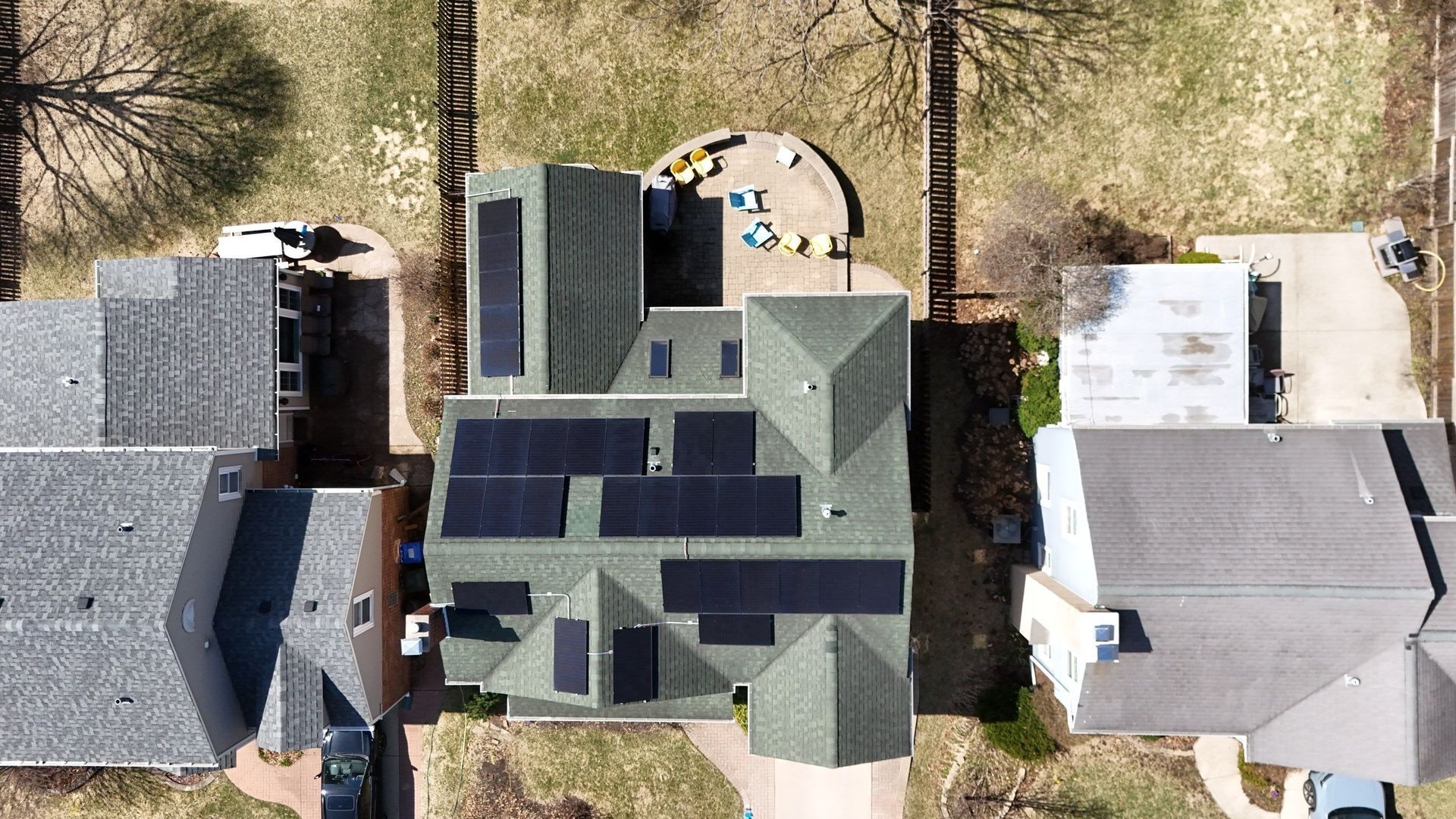 Overhead view of a house with solar panels on the green roof, surrounded by other houses and trees.