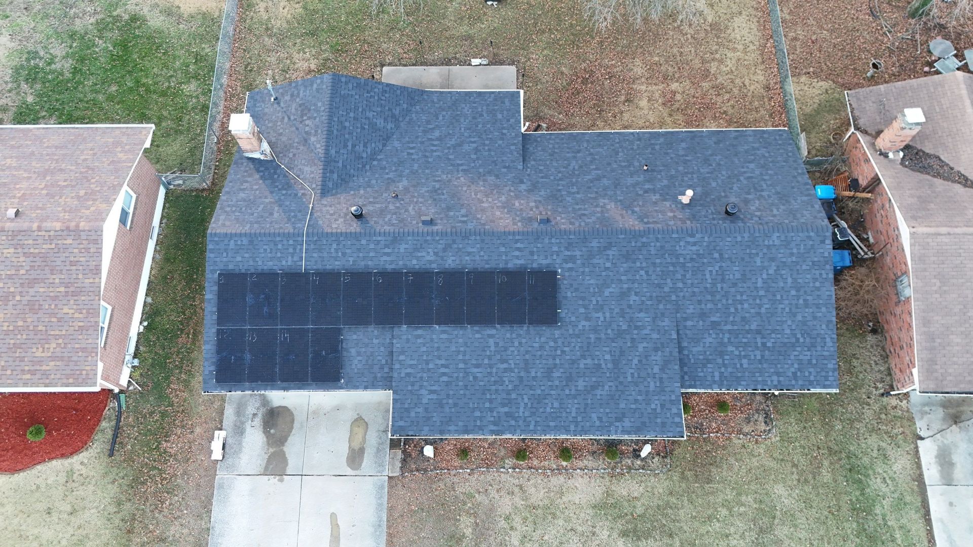 Overhead view of a house with solar panels on the roof; surrounded by other houses, grass, and concrete.