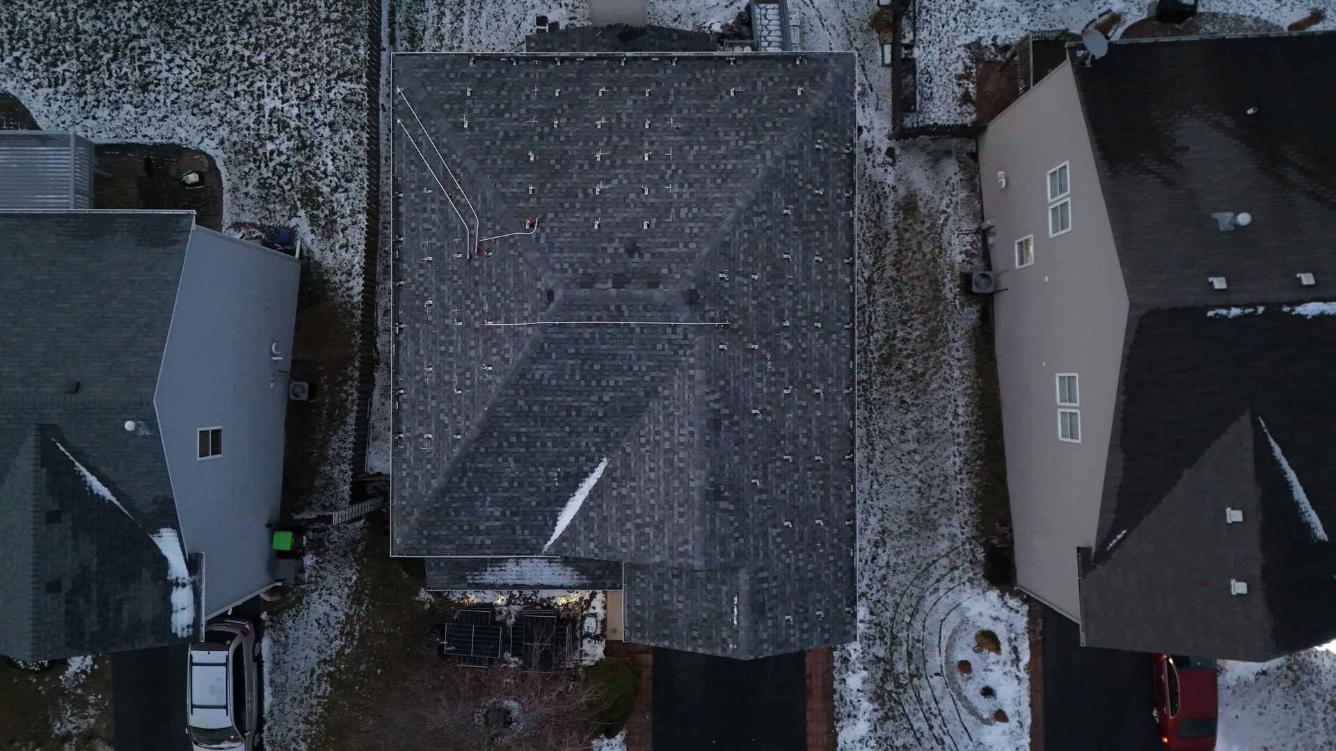 Overhead view of three houses with snow-covered roofs and yards in a residential neighborhood.
