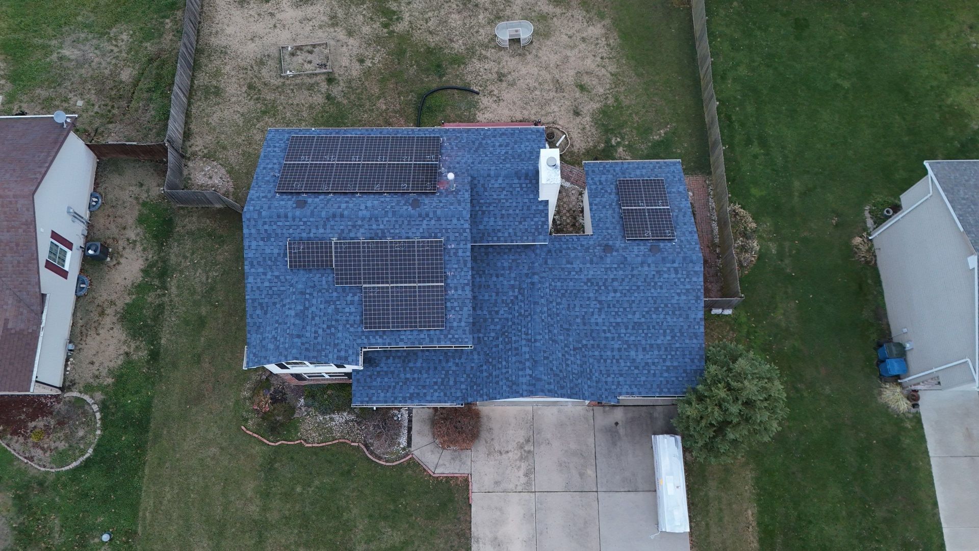 Overhead view of a house with solar panels on the blue roof. Green grass surrounds the house.