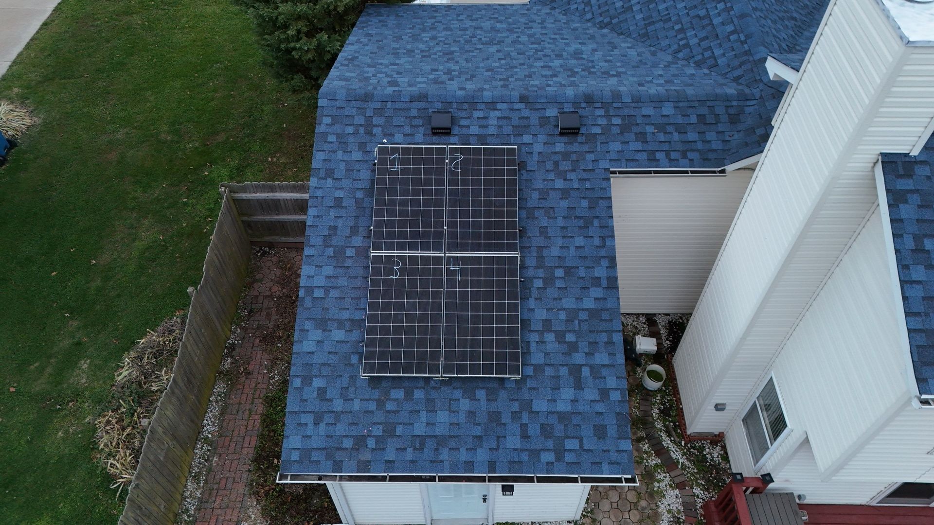 Overhead view of a house roof with solar panels; panels have weathered areas. Blue shingles.