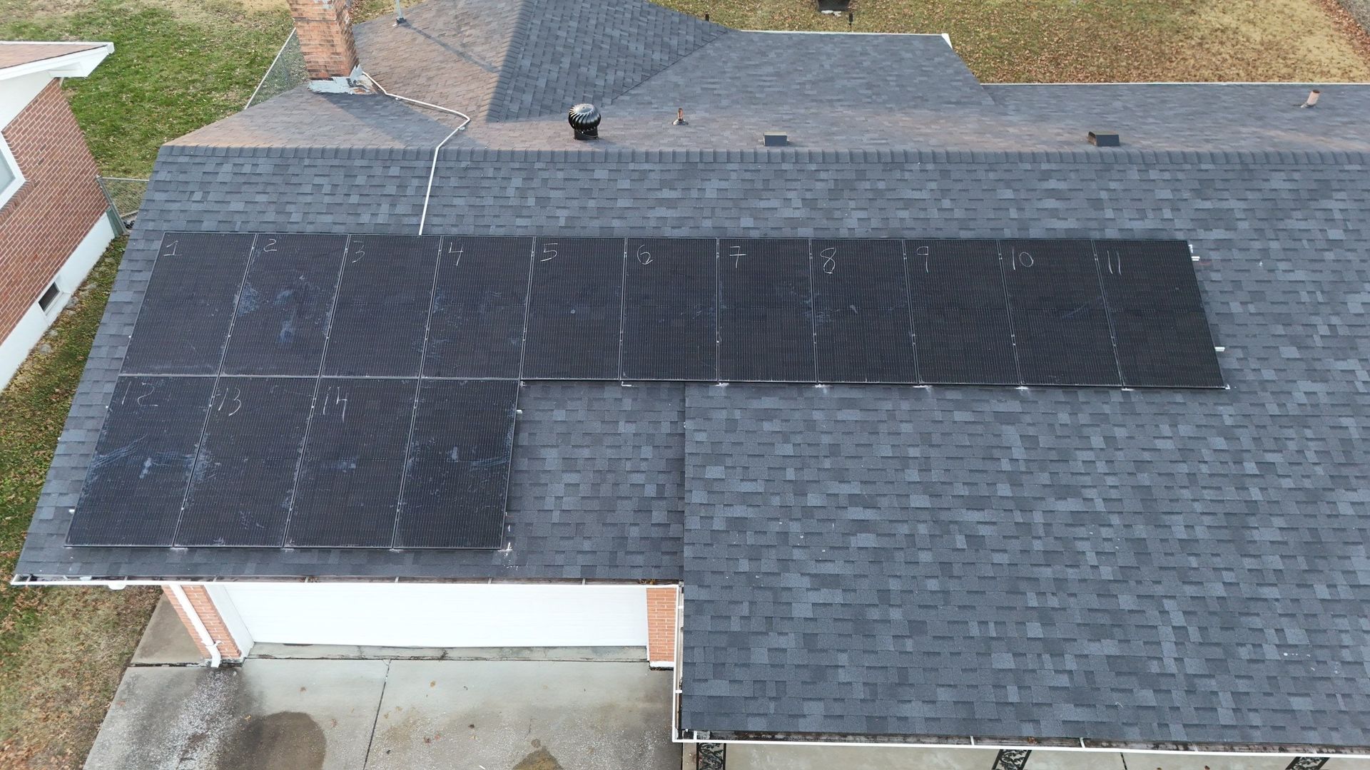 Solar panels on a residential roof with dark shingles, seen from an aerial perspective.