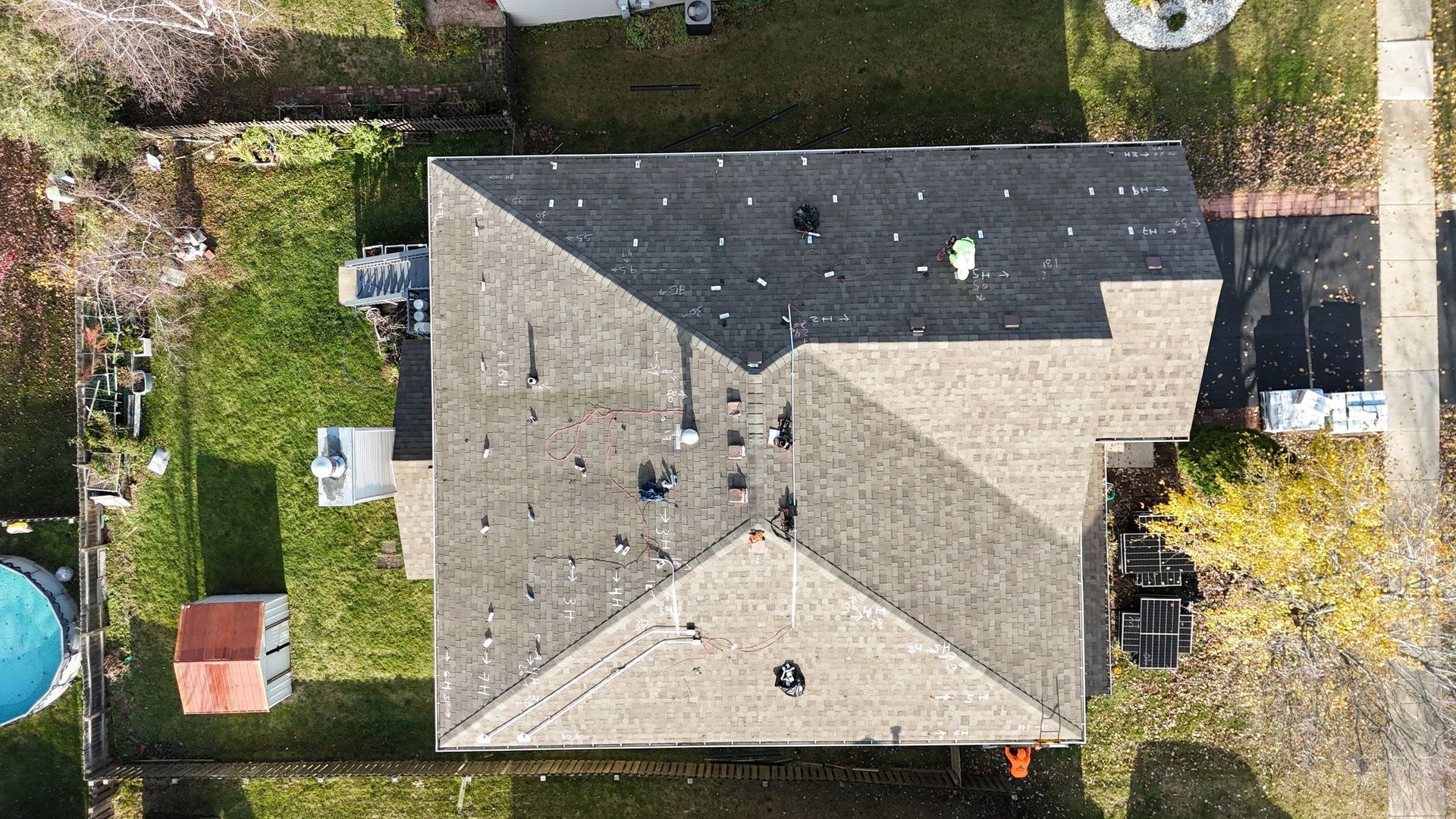 Overhead view of a house with a weathered, gray roof, surrounded by grass, trees, and a small pool.