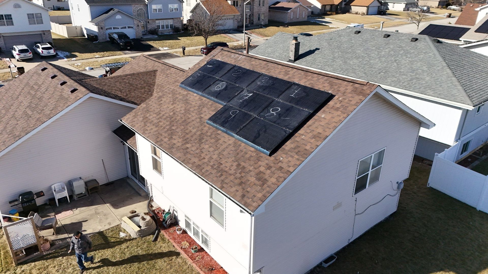 An aerial view of a house with solar panels on its roof. The roof is brown, with a white house and backyard.