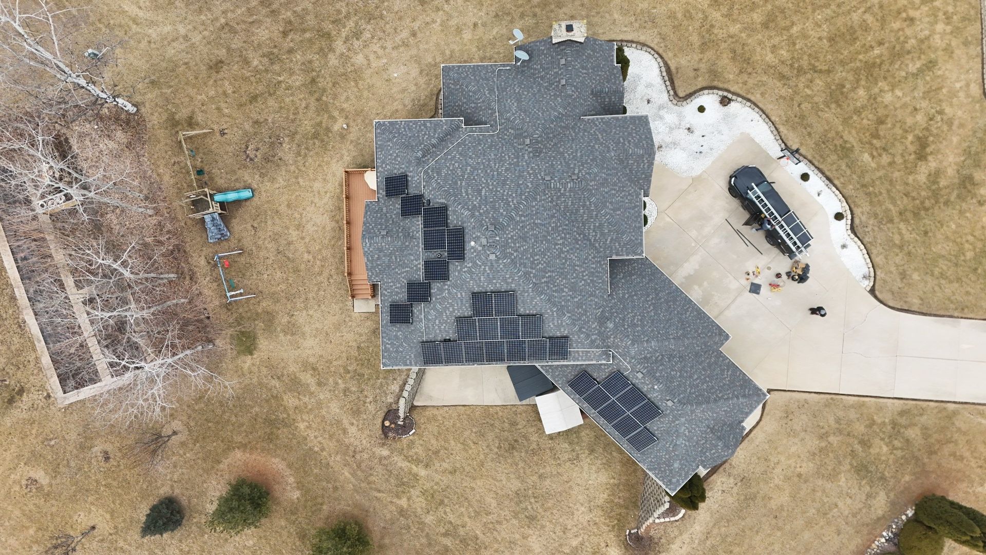 Overhead view of a house with solar panels on its roof, concrete driveway, and surrounding lawn.