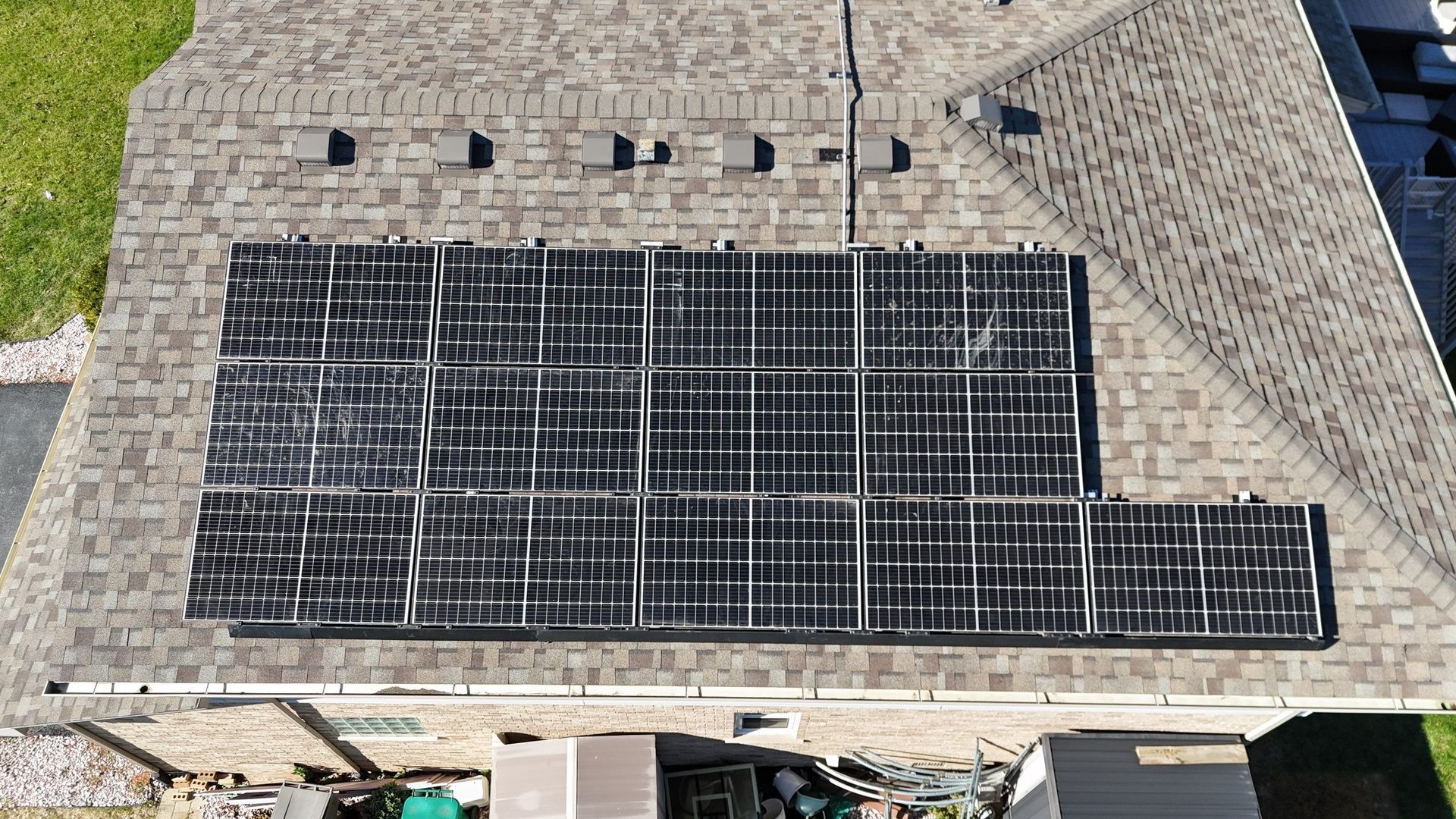 Aerial view of a house with solar panels installed on its brown shingle roof.