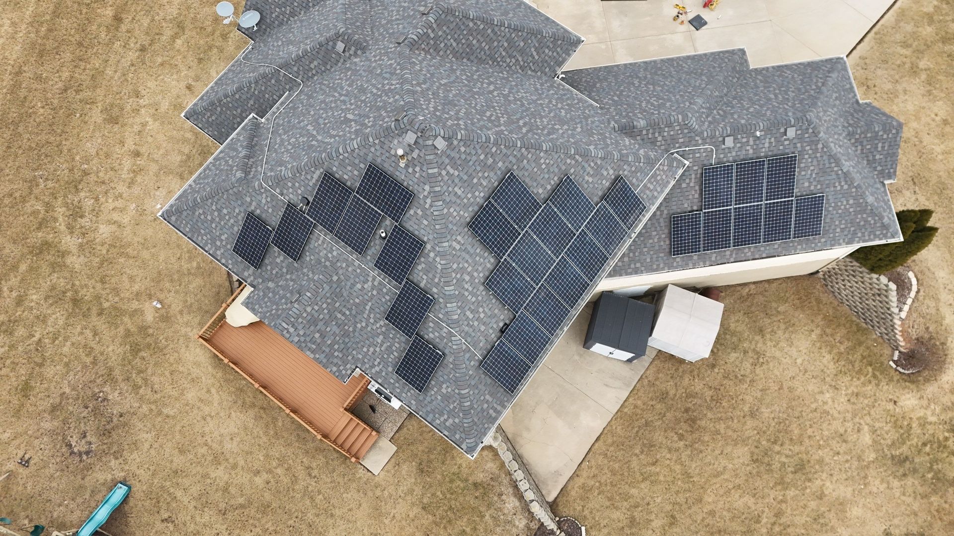 Overhead view of house with dark solar panels on gray shingled roof, set on brown grassy landscape.