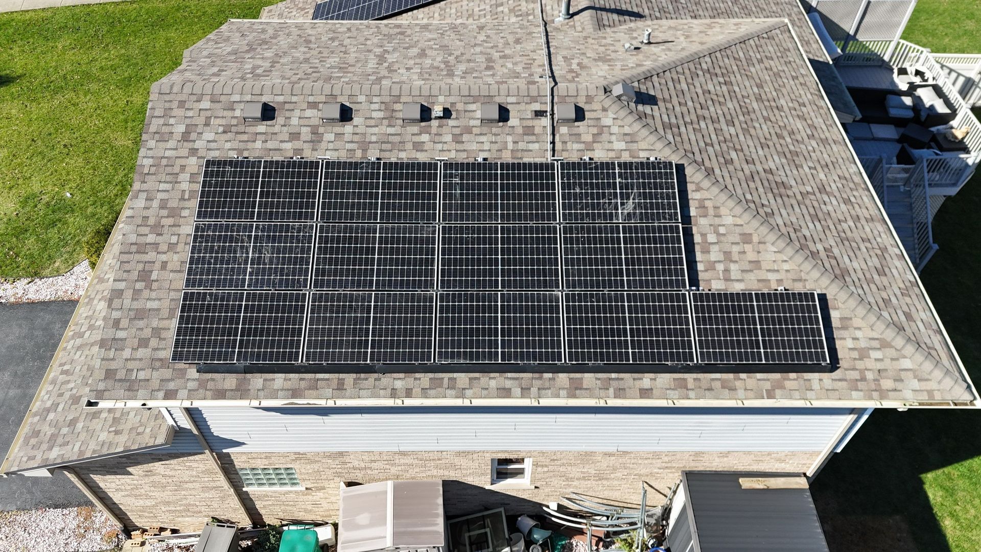 Solar panels installed on a shingled roof of a house; green lawn and partial siding are visible.