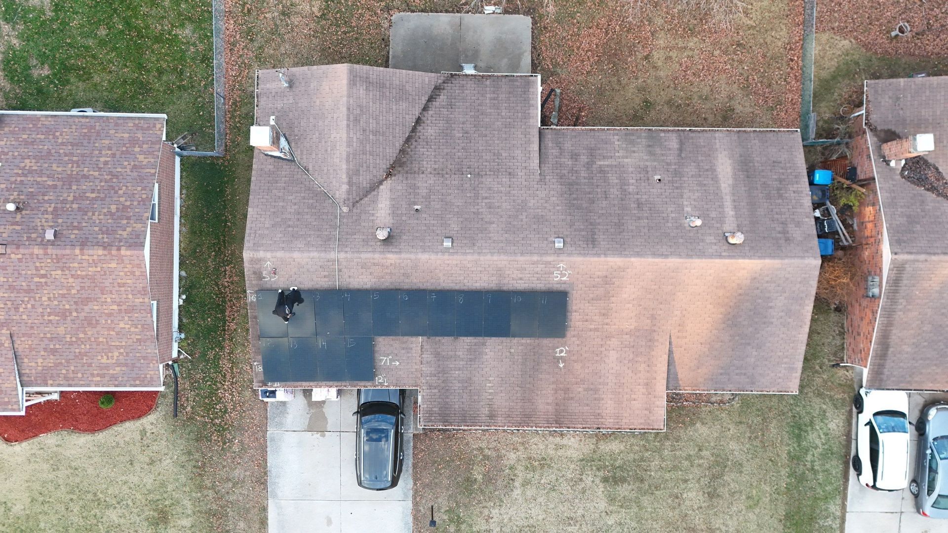Aerial view of a house with solar panels, a car in the driveway, and neighboring houses.