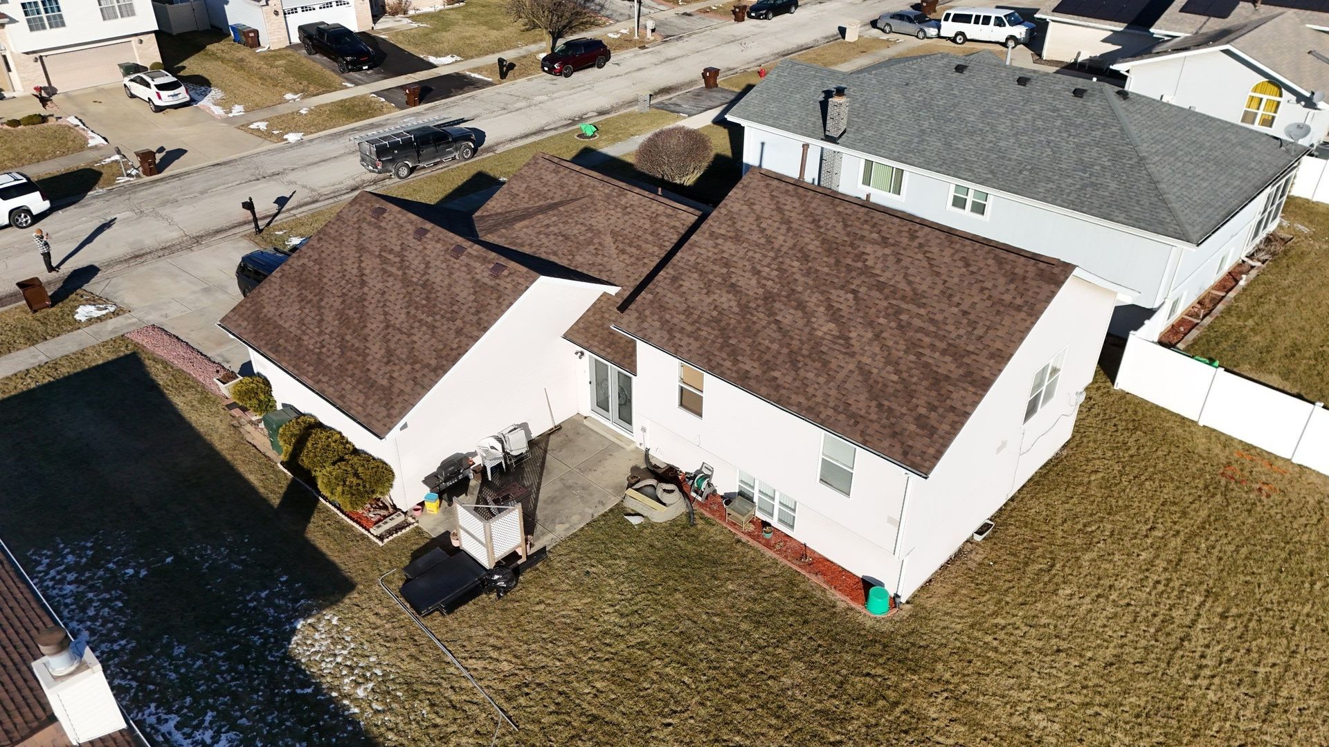 Aerial view of a two-story beige house with a brown roof and a backyard on a sunny day.