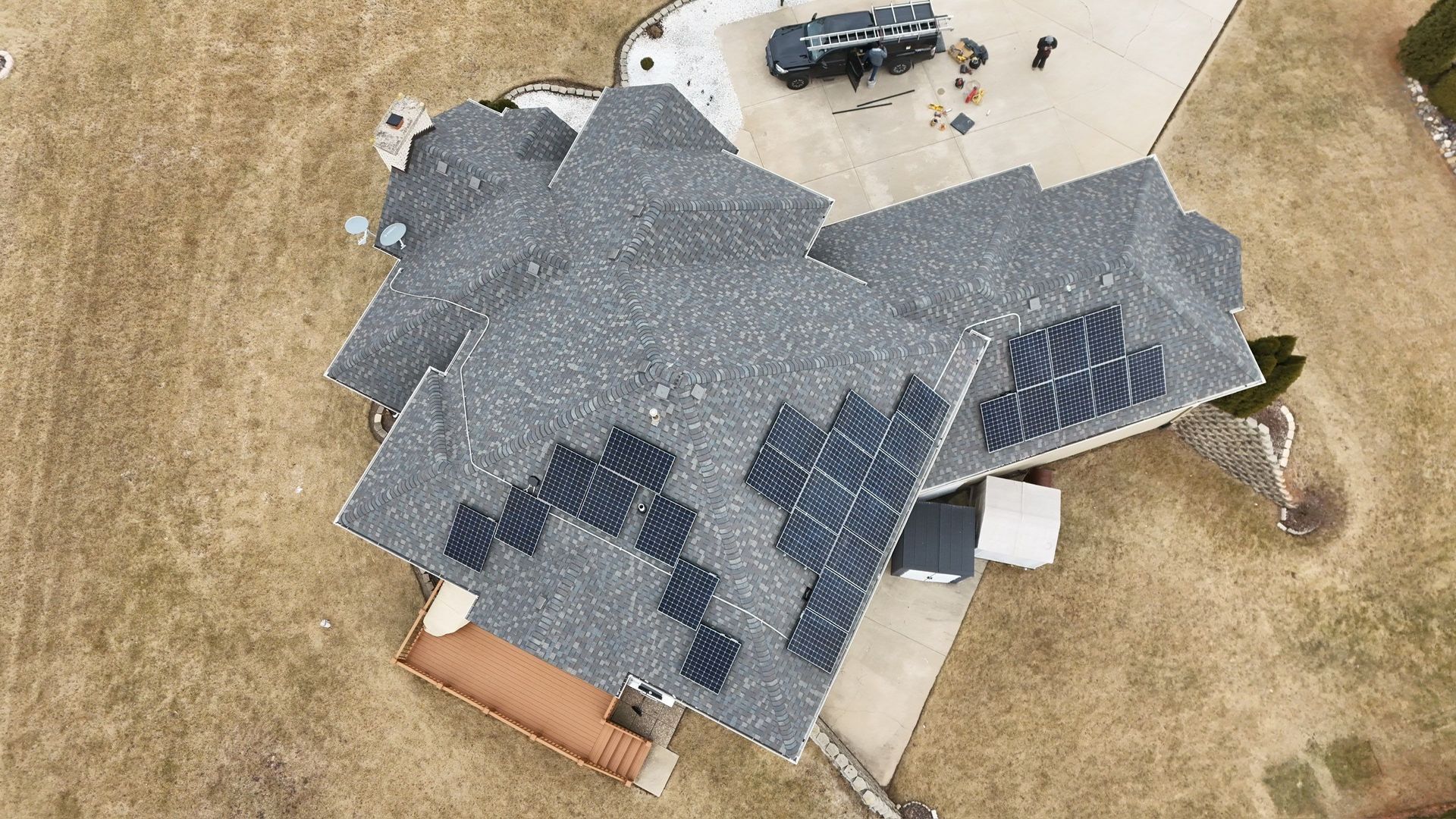 Aerial view of house with gray roof and solar panels on brown grass.