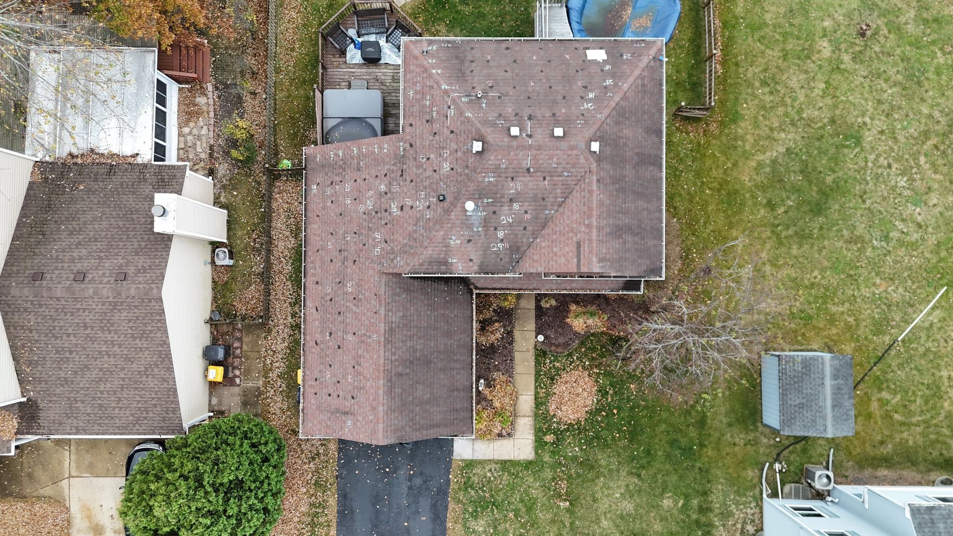 Aerial view of two houses with brown roofs surrounded by greenery and pavement.