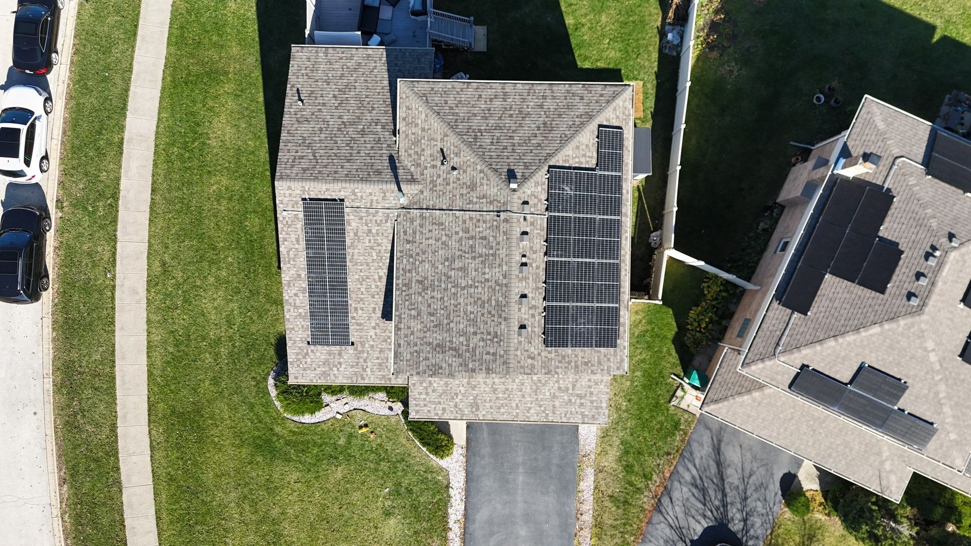 Overhead view of a house with solar panels on the roof, driveway, and surrounding grass.