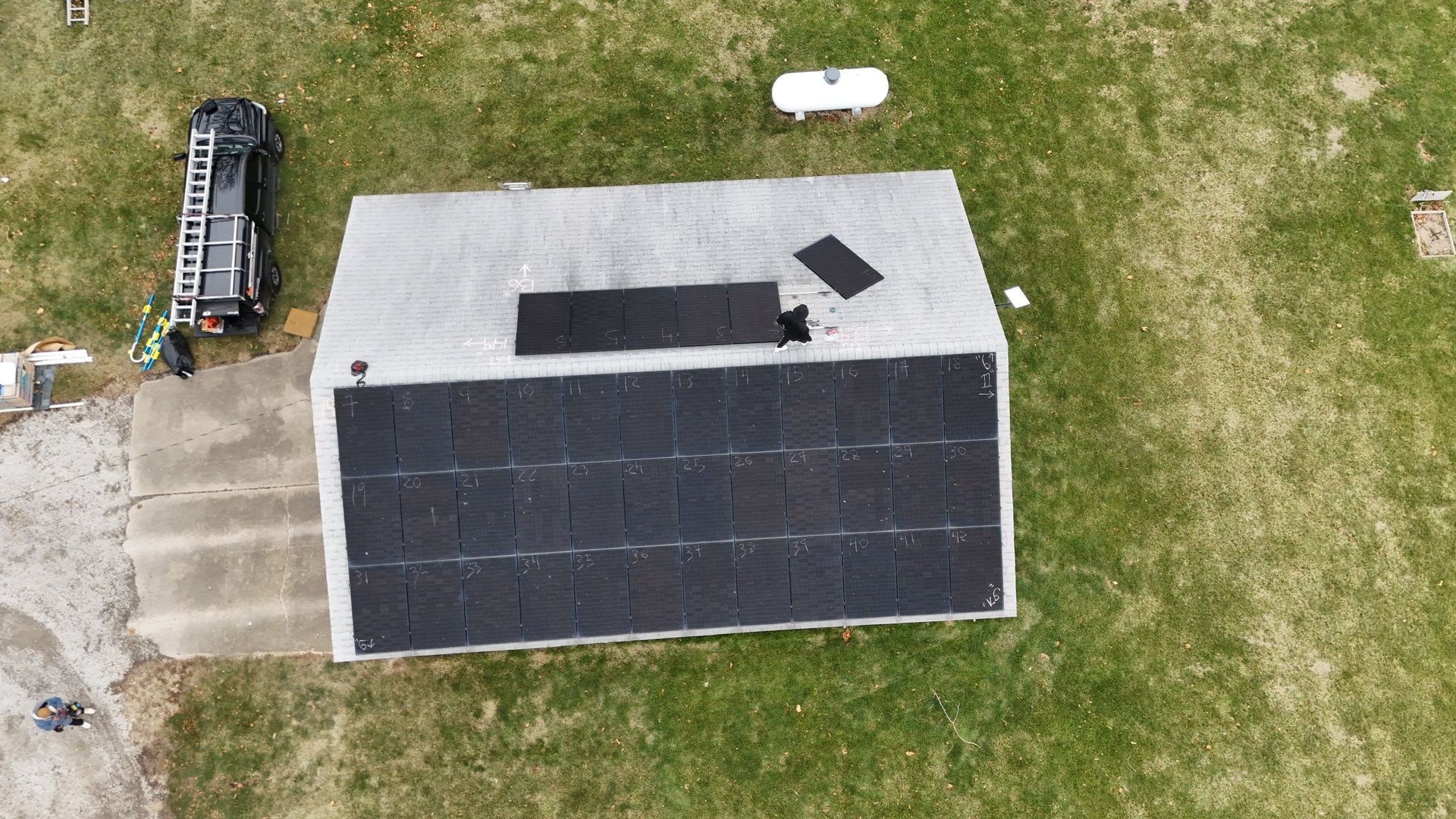 Aerial view of a house with solar panels, a partially damaged roof, and a fire truck parked nearby.
