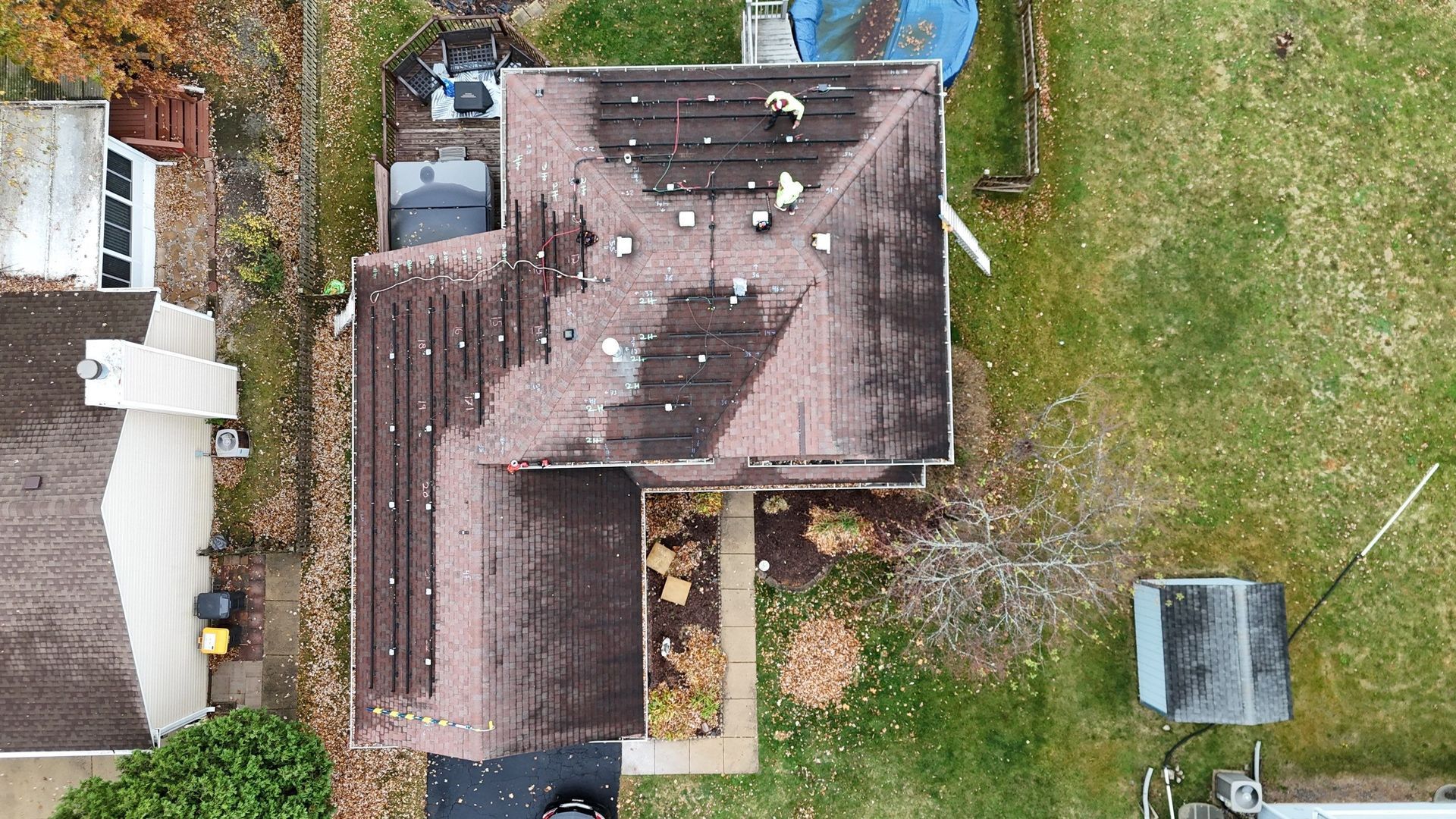 Overhead view of a house roof with brown shingles, visible vents, and a person working on the roof.