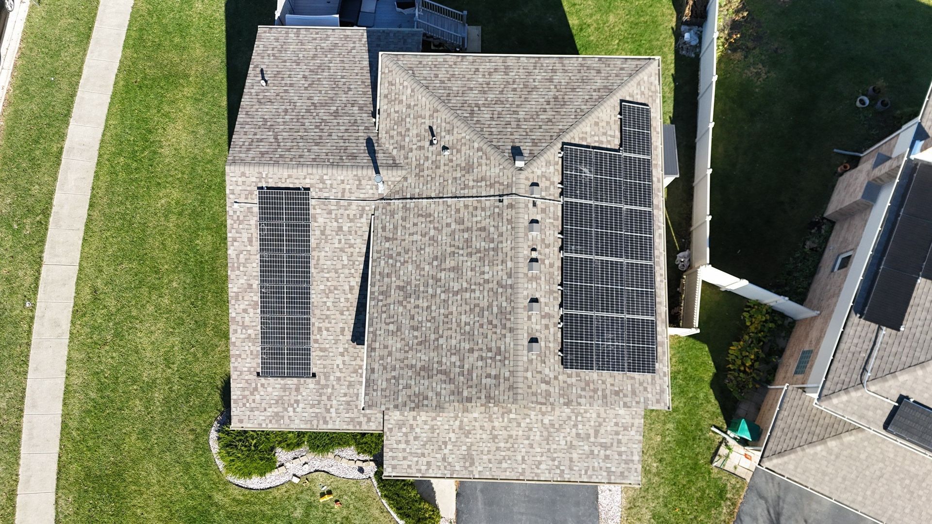 Overhead view of a house with solar panels on the roof, surrounded by green grass and a paved driveway.