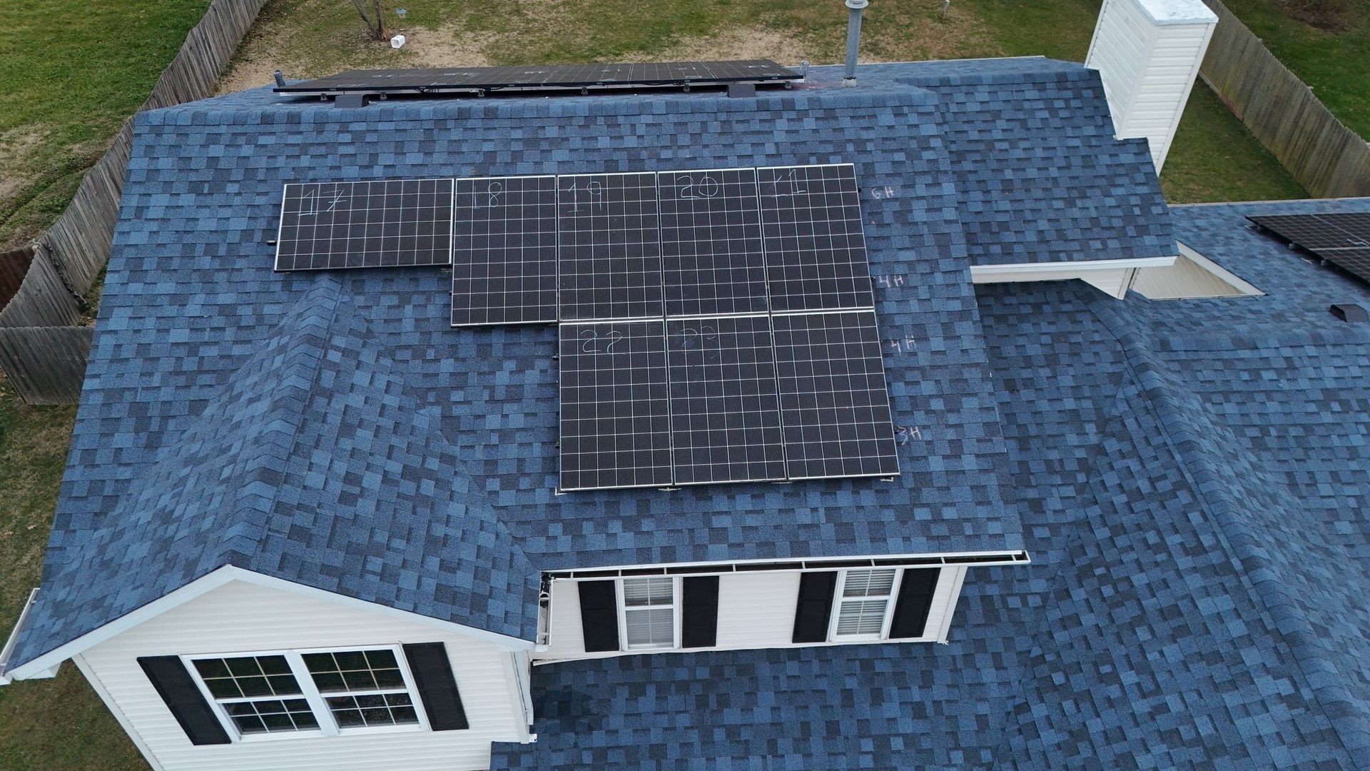 Blue shingled roof with faded solar panels; white house with black shutters; aerial view.