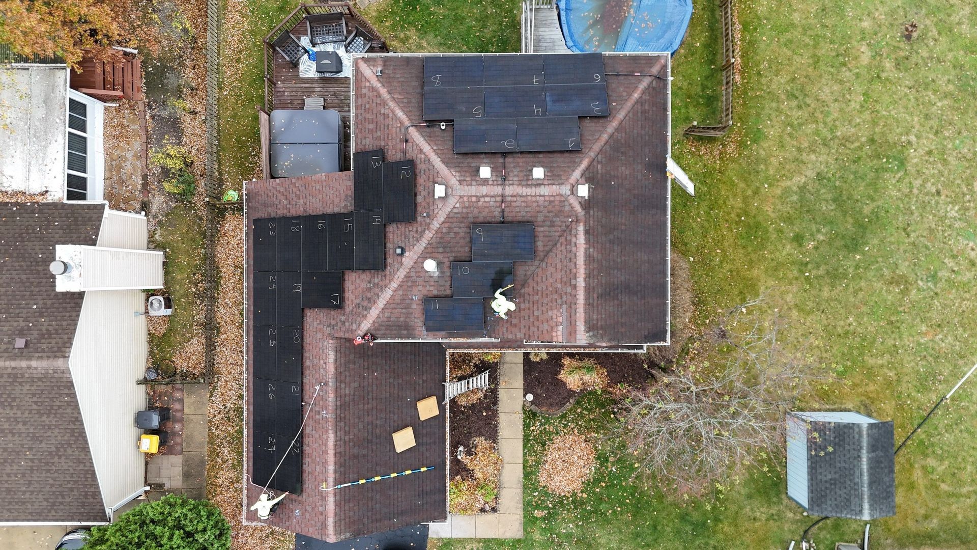 Overhead view of a house roof with dark patches of solar panels on a cloudy day.