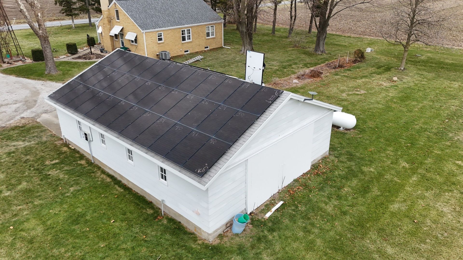 A white building with solar panels on the roof, located in a grassy field with a yellow building in the background.