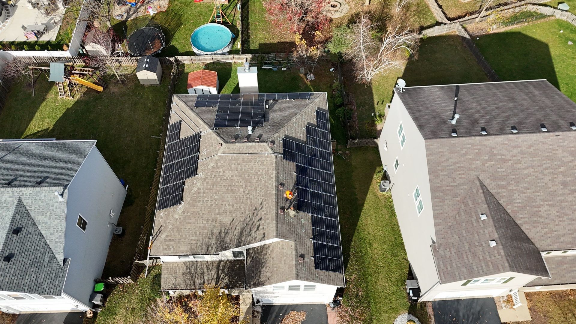 Aerial view: House with solar panels on roof, surrounded by other houses and green lawns.