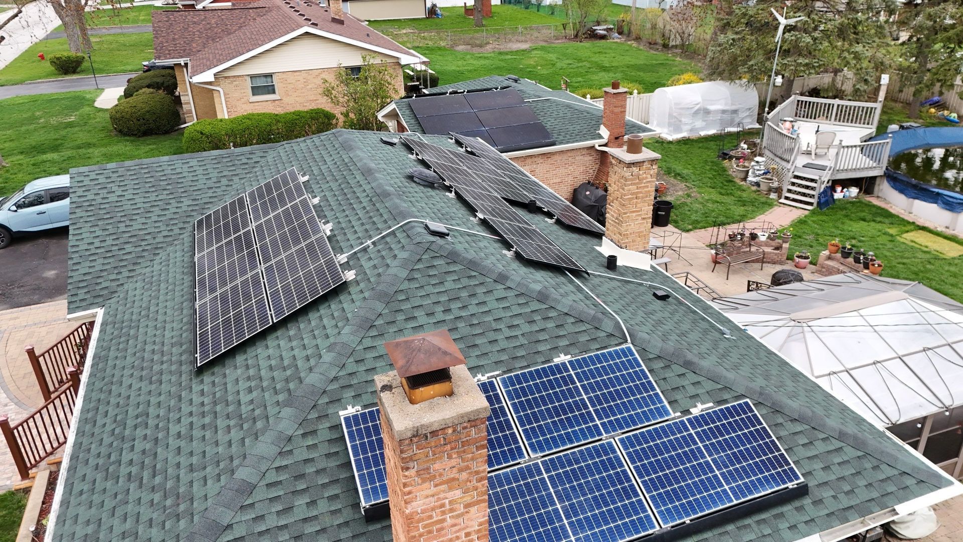 Solar panels on a residential roof, capturing sunlight for energy. Green roof, brick chimneys, suburban setting.