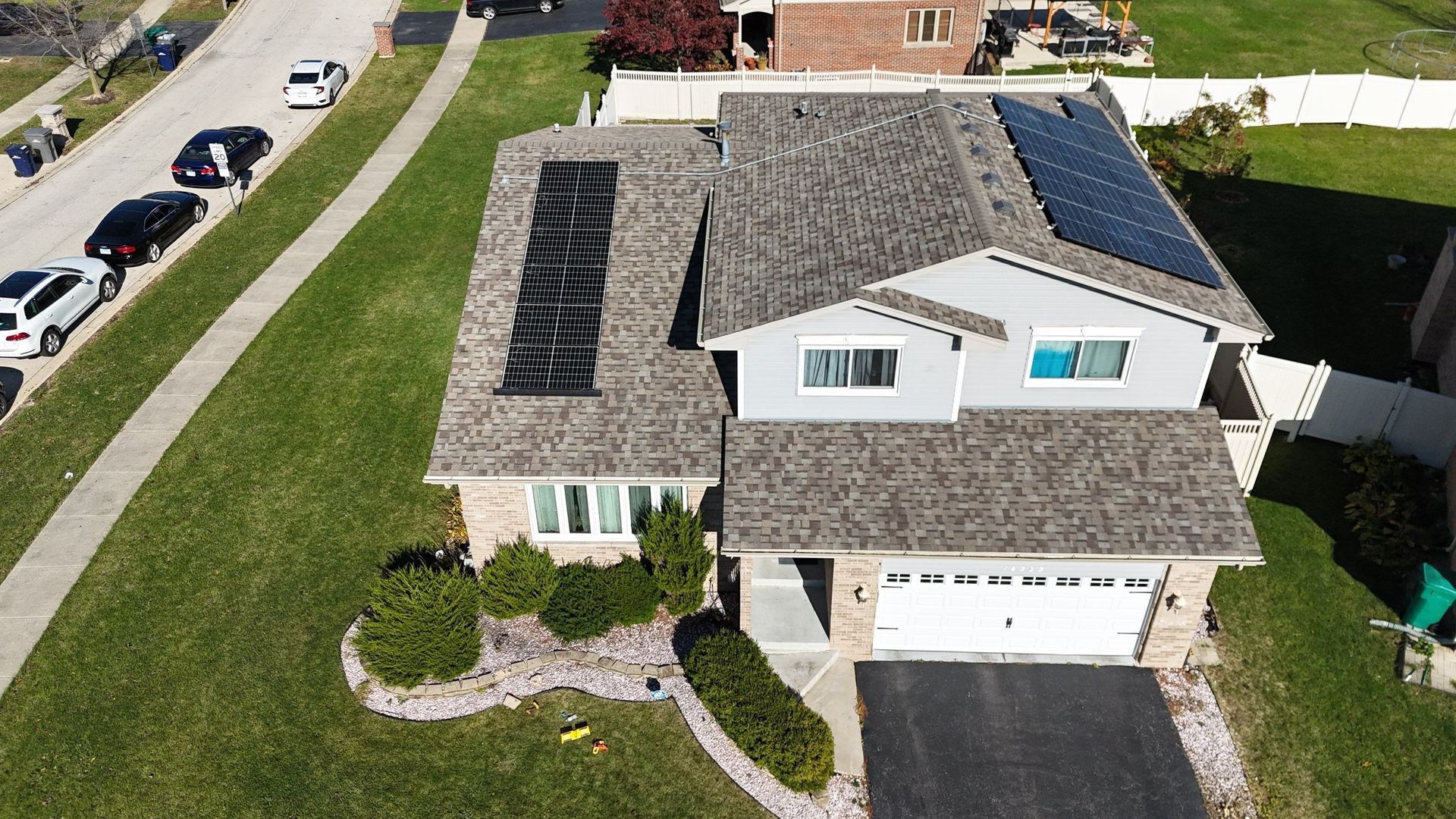 Residential house with solar panels on the roof, surrounded by green lawn and a street.