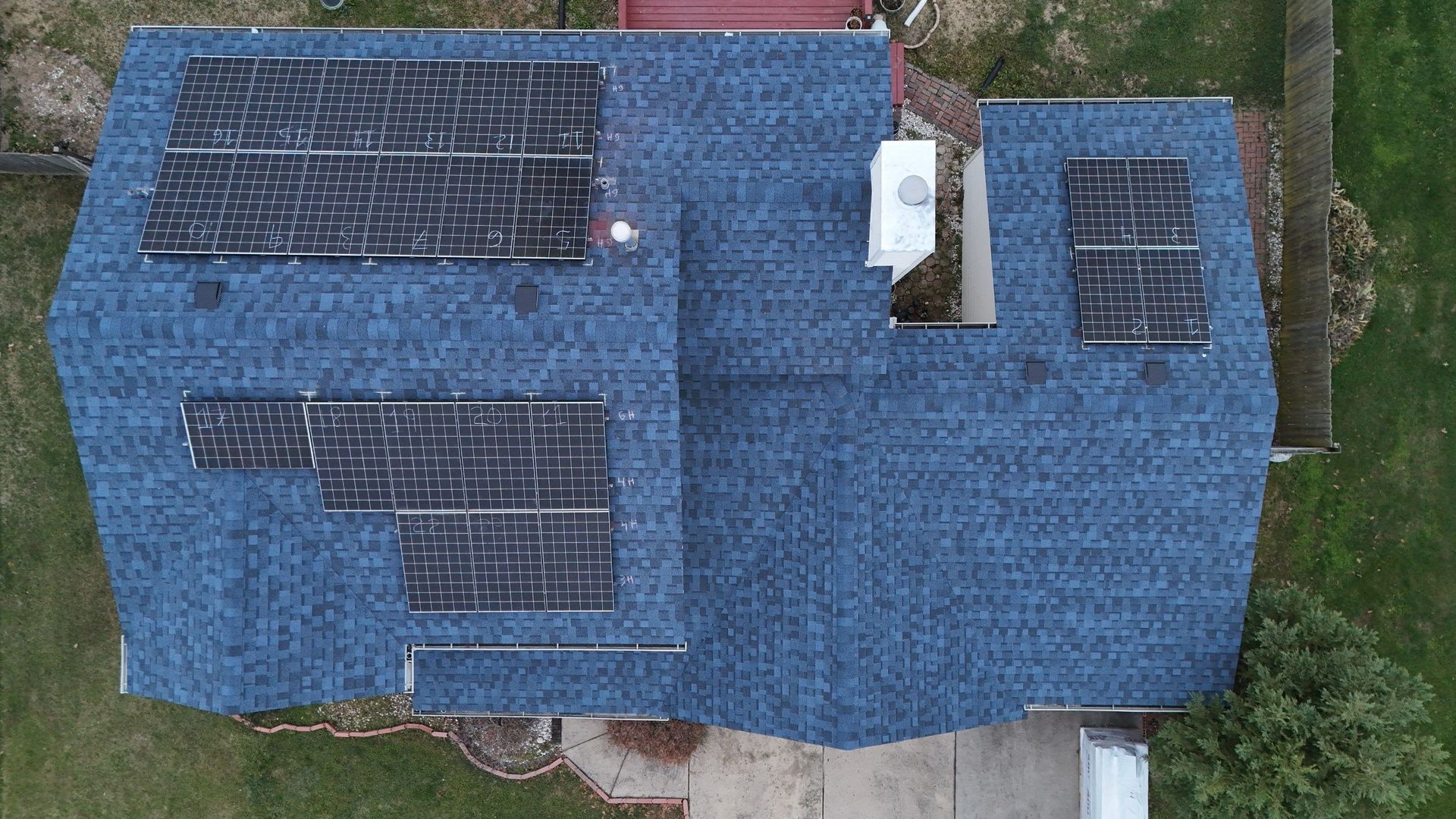 Aerial view of a blue-roofed house with solar panels on the roof.