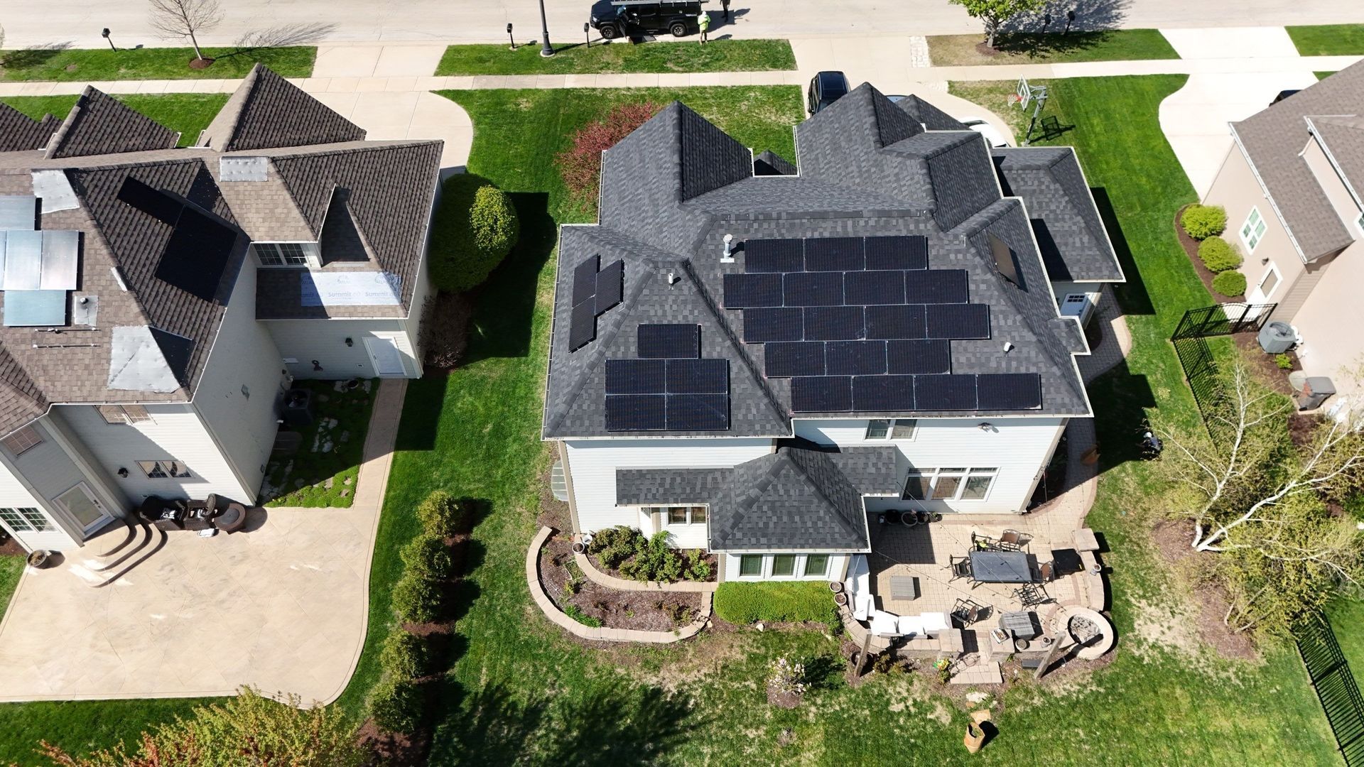 Overhead view of a white house with a dark roof covered in solar panels, with a lawn and neighboring houses.