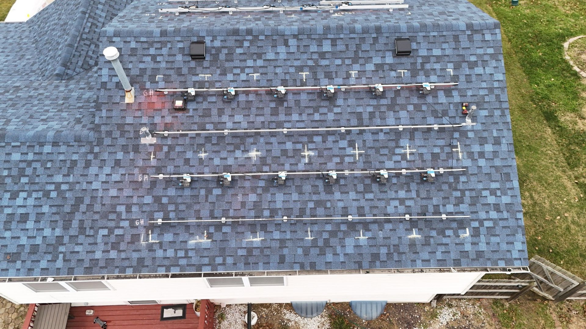 Rooftop solar panels installed on a blue shingled roof.  Surrounding grass and a deck visible.