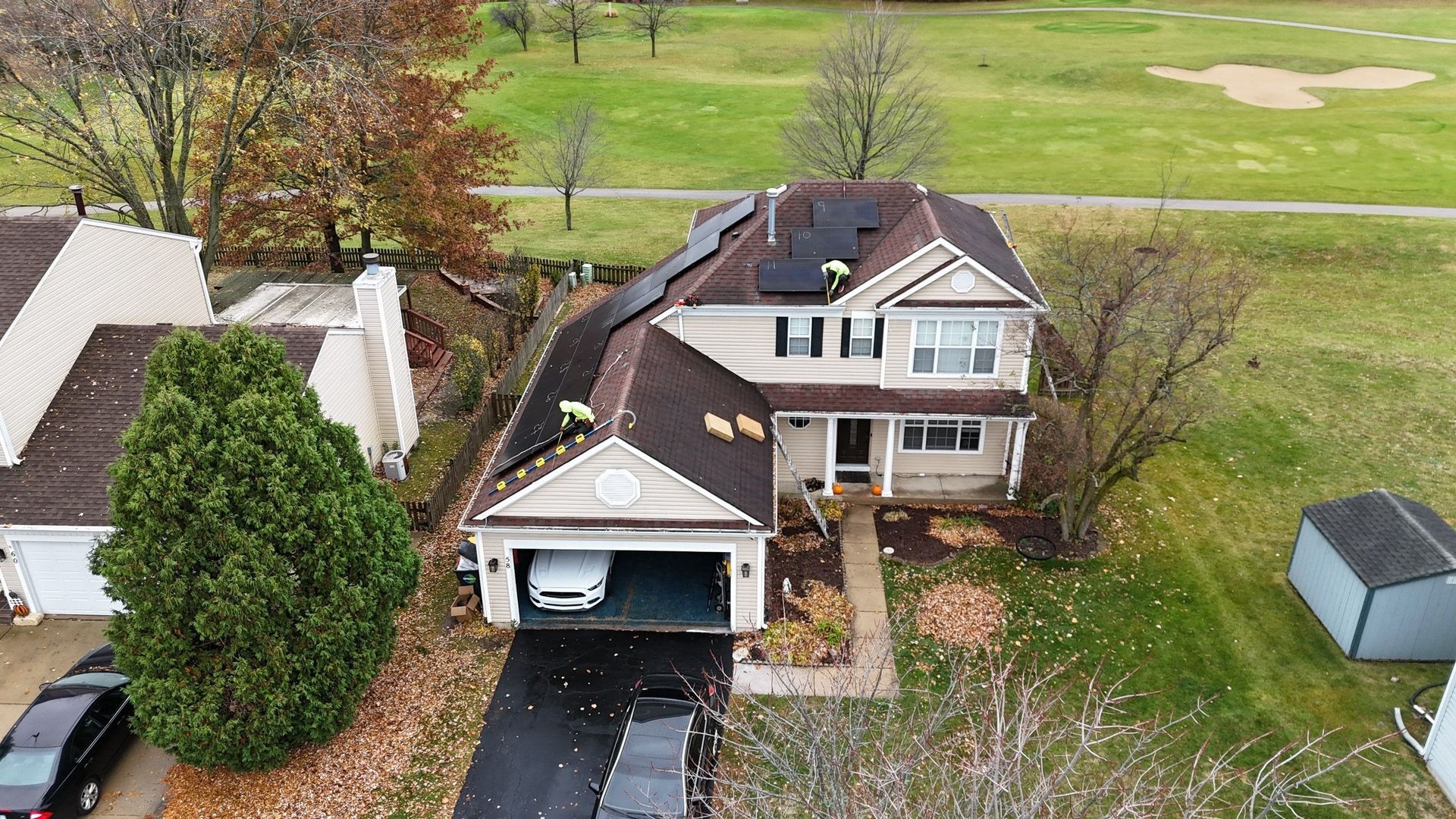 House with solar panels, garage, and a driveway, next to a golf course. Cloudy, autumn day.