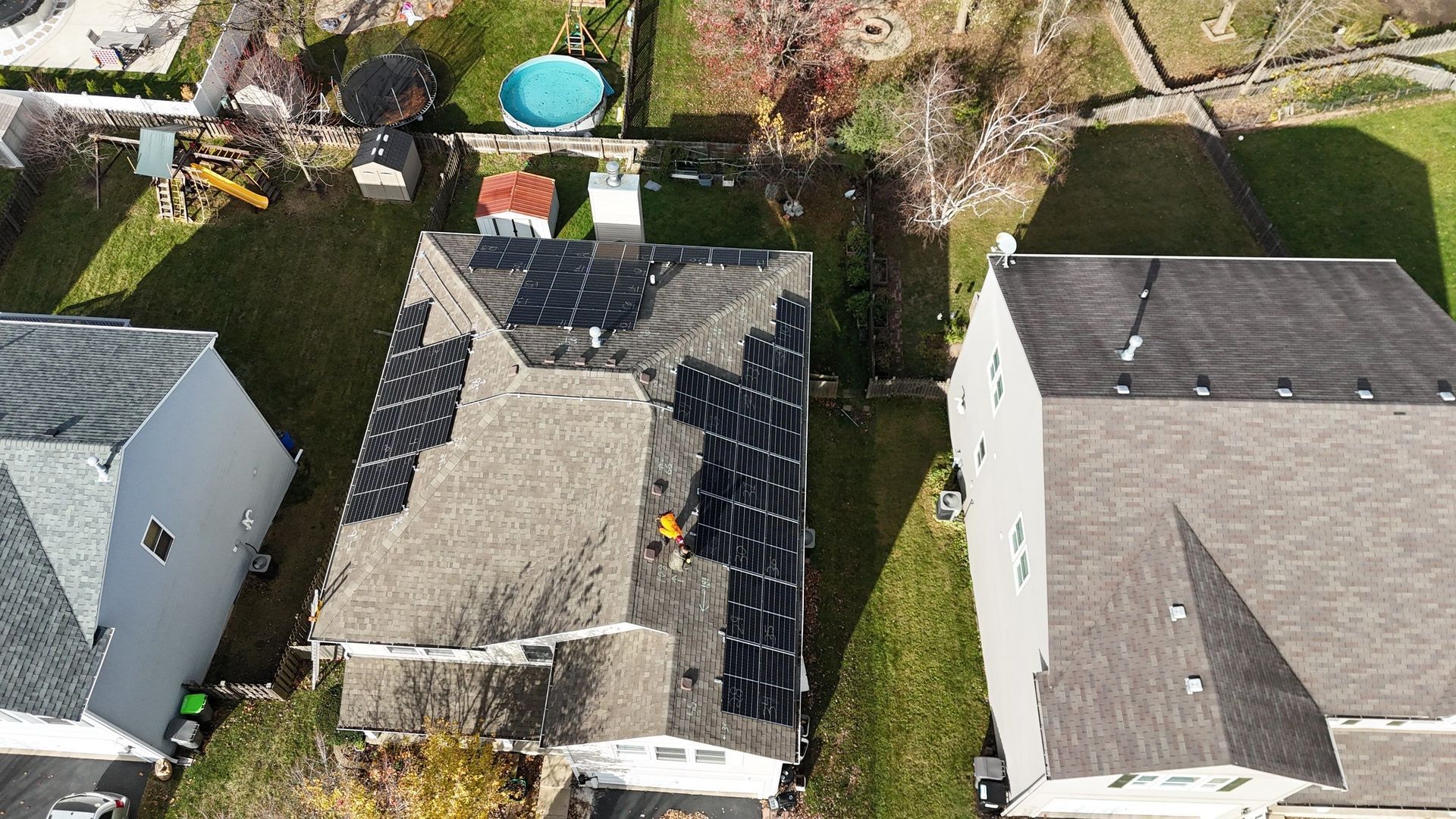 Aerial view of a house with solar panels on the roof, surrounded by other houses and green lawns.