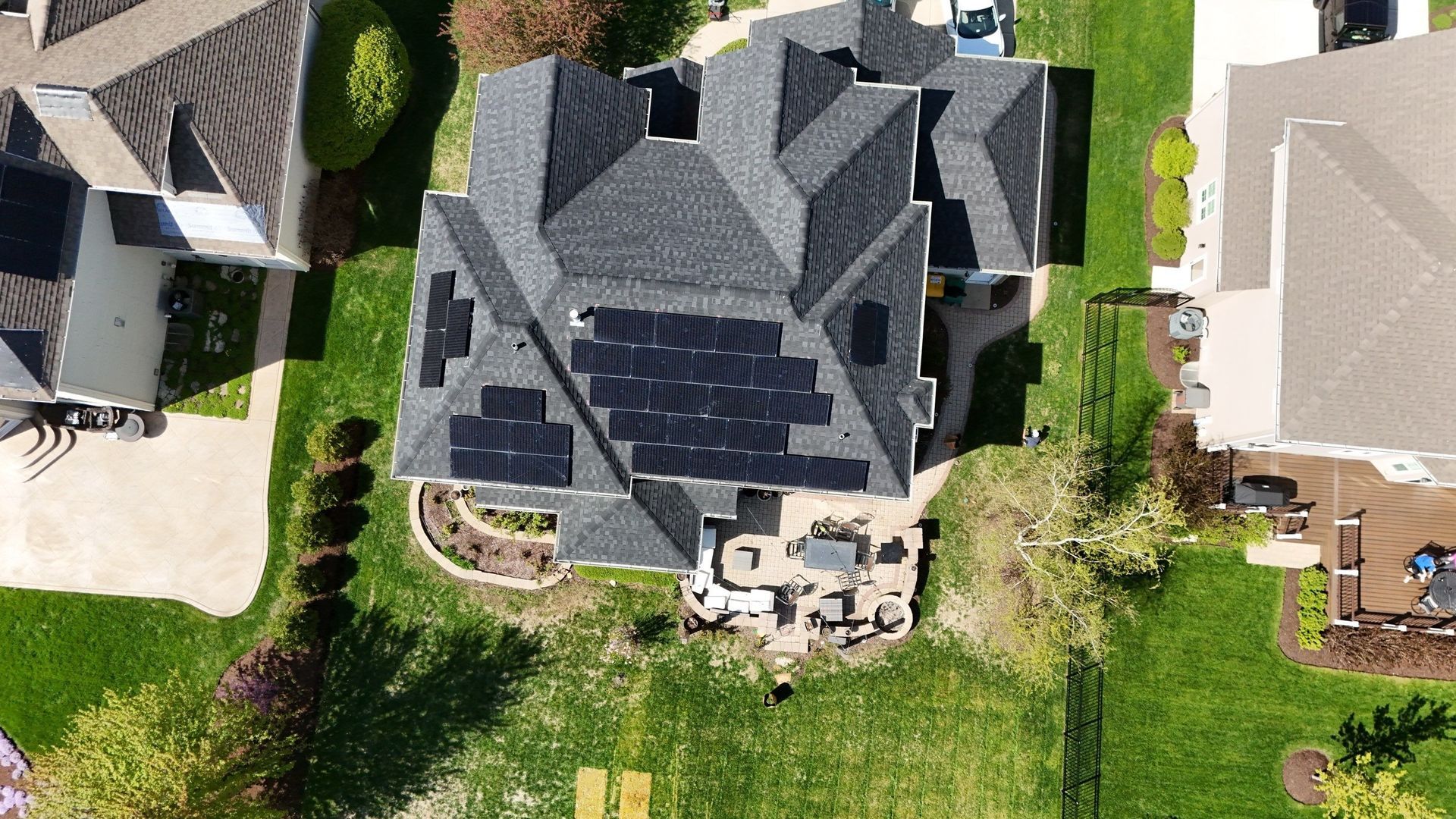 Aerial view of house with solar panels on the roof, surrounded by green lawn and other houses.