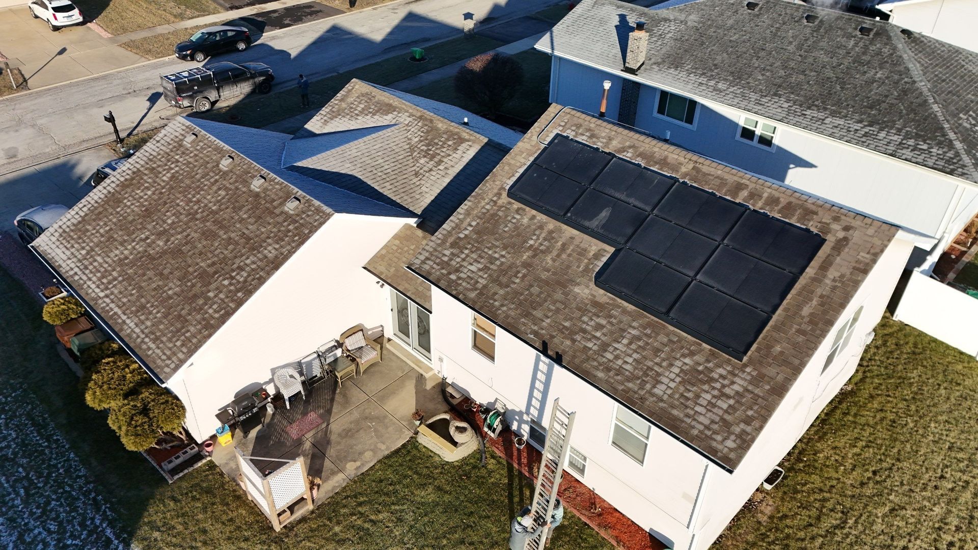 Overhead view of a house with solar panels on the roof; a ladder and a nearby street.