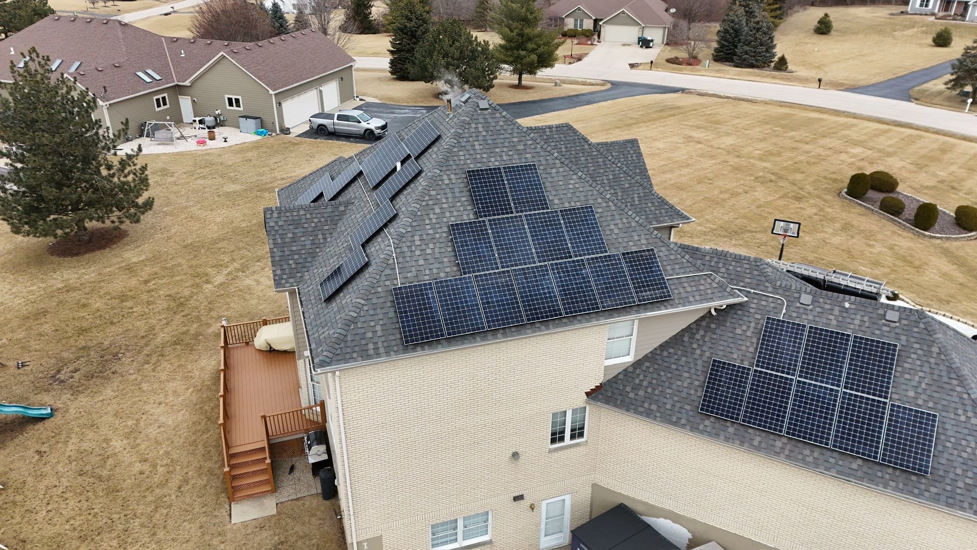 Solar panels installed on a residential house roof. Brown, gray, and black colors. Overlooking a suburban setting.