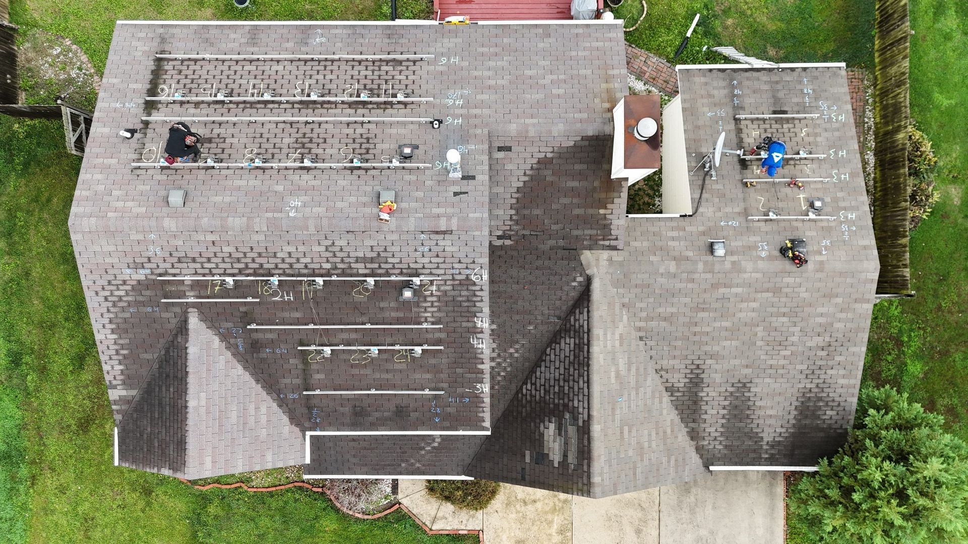 Overhead view of two roofers installing solar panels on a gray shingled roof.