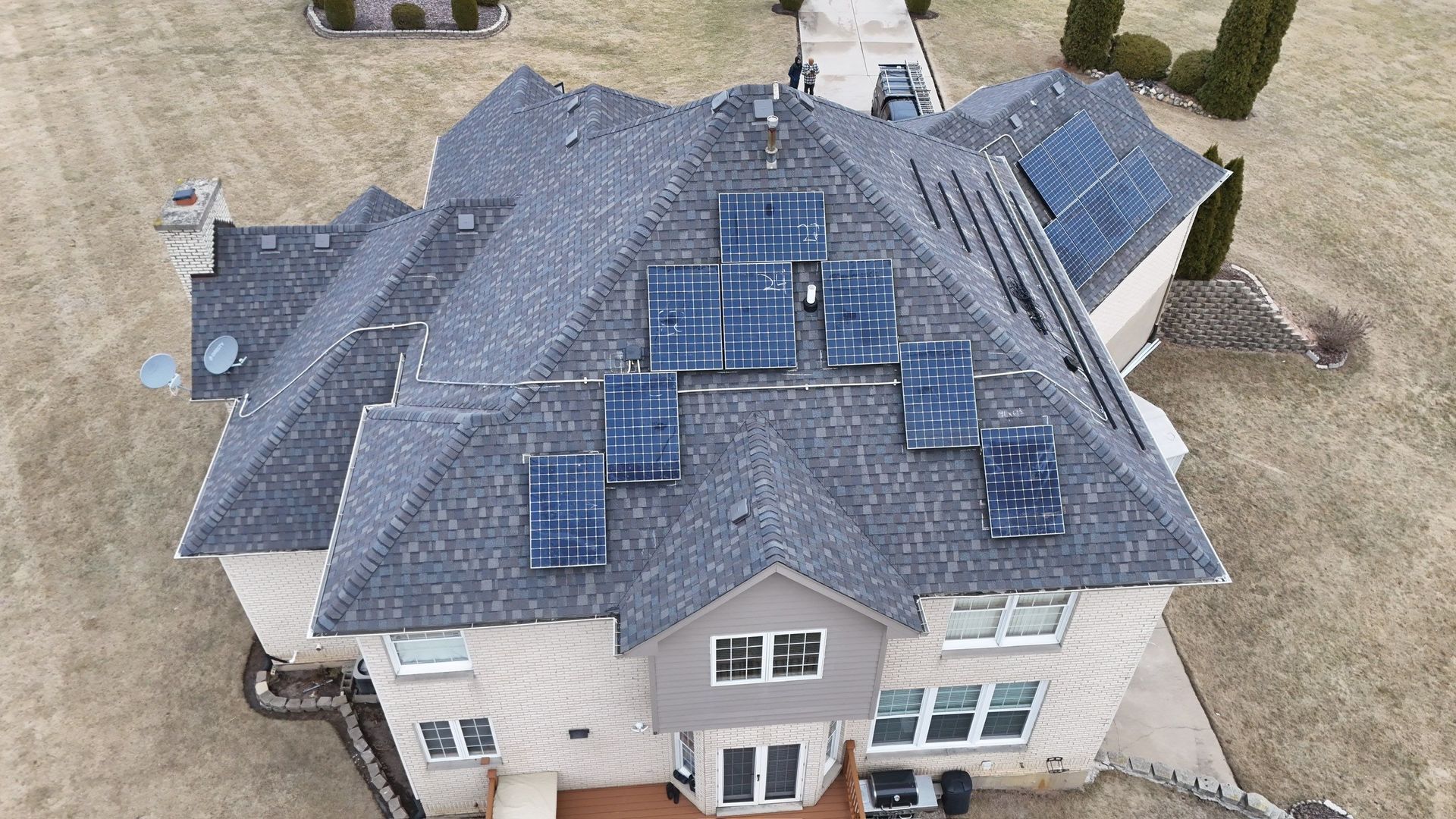 Aerial view of a house with solar panels on its roof, set in a yard with brown grass.