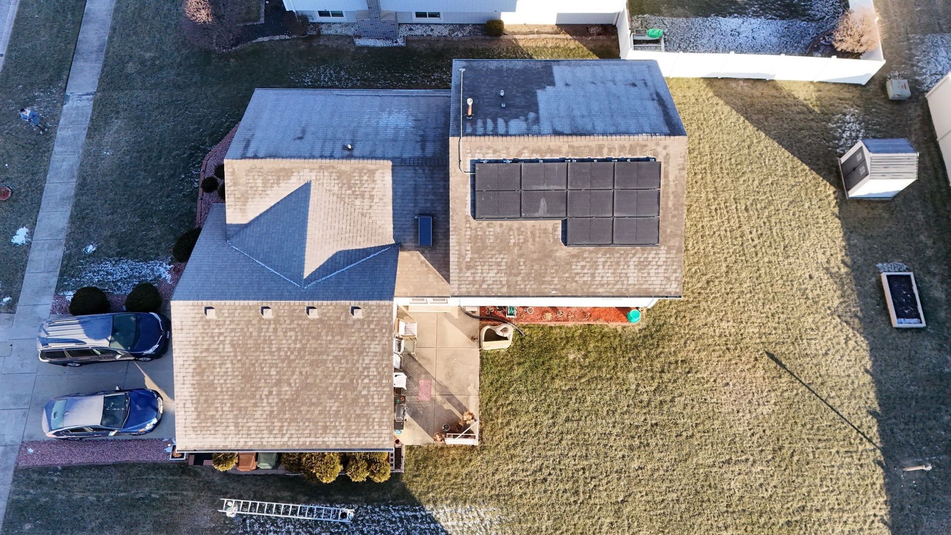 Overhead view of a house with solar panels on the roof, cars in the driveway, and a grassy yard.