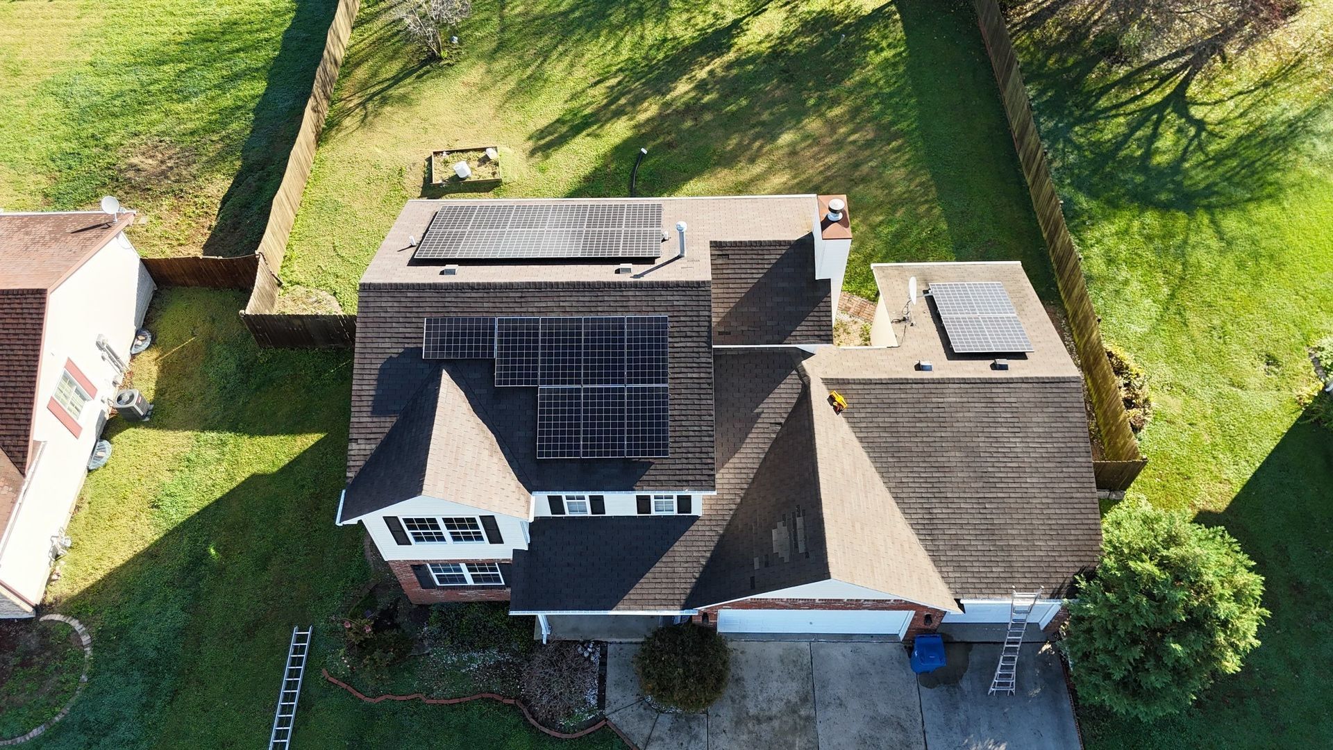 Aerial view of a house with solar panels on its roof, surrounded by a green lawn.