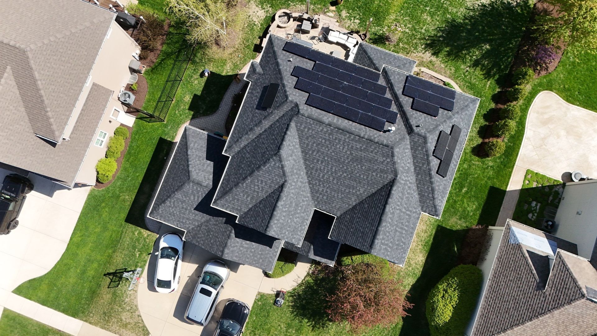 Aerial view of a house with solar panels on the roof, surrounded by green lawn and other houses.