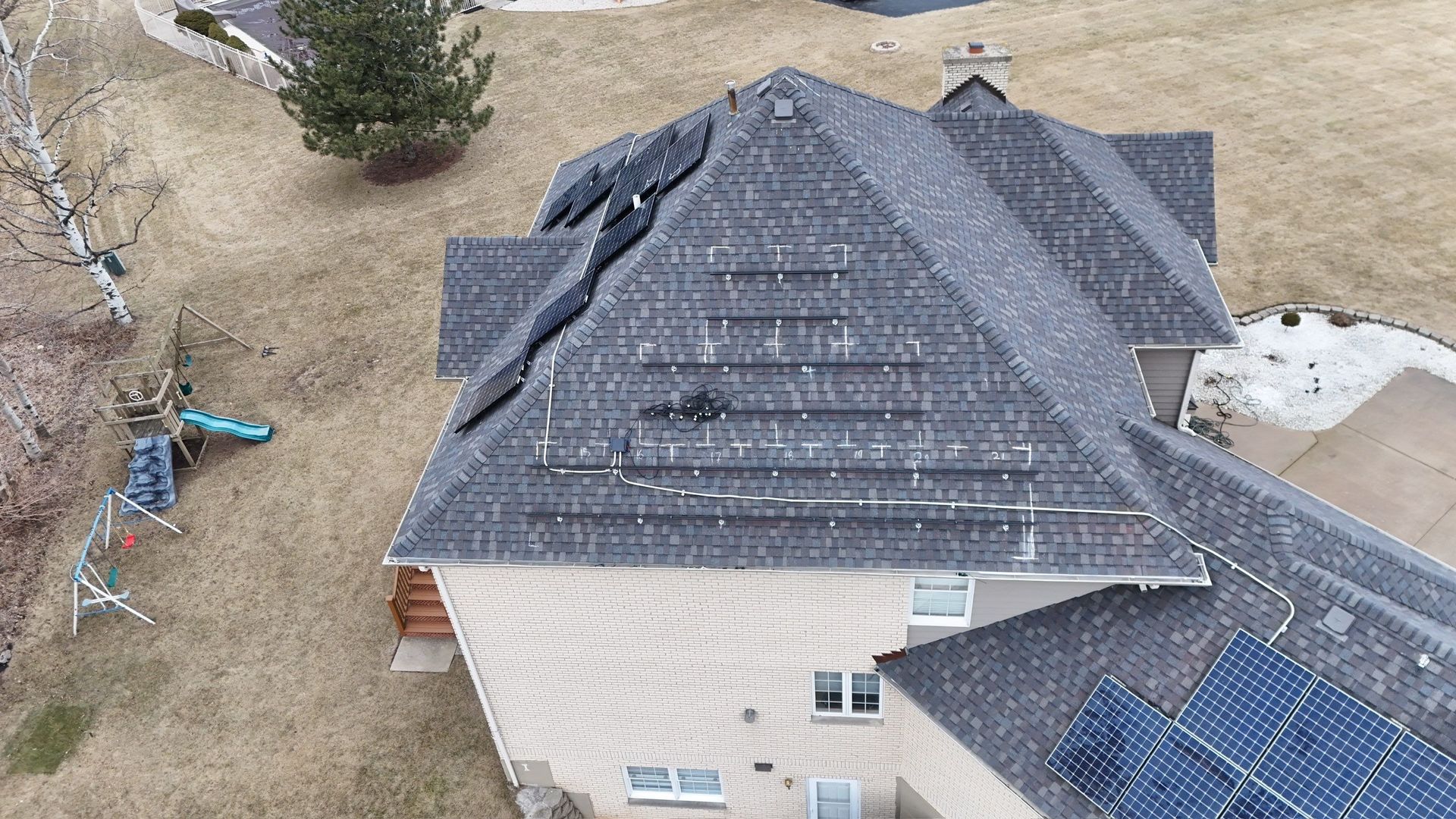 Overhead view of a house with solar panels on the roof. The roof is gray, and the surrounding area is brown grass.