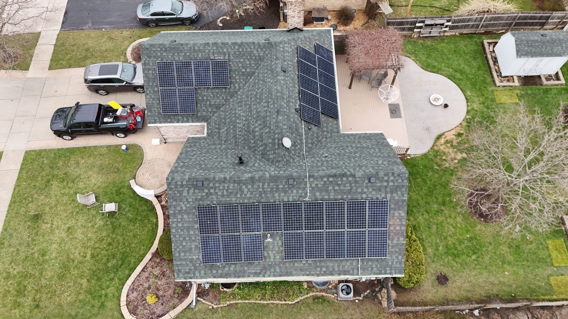 Overhead view of a house with solar panels on the roof; a truck, cars, and a patio are nearby.