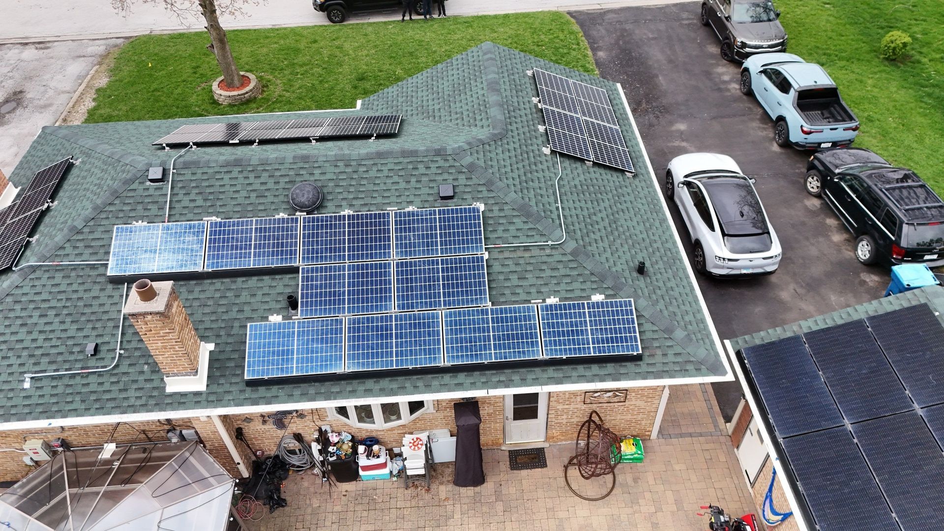 Overhead view of a house with solar panels on a green roof, cars parked on the street.
