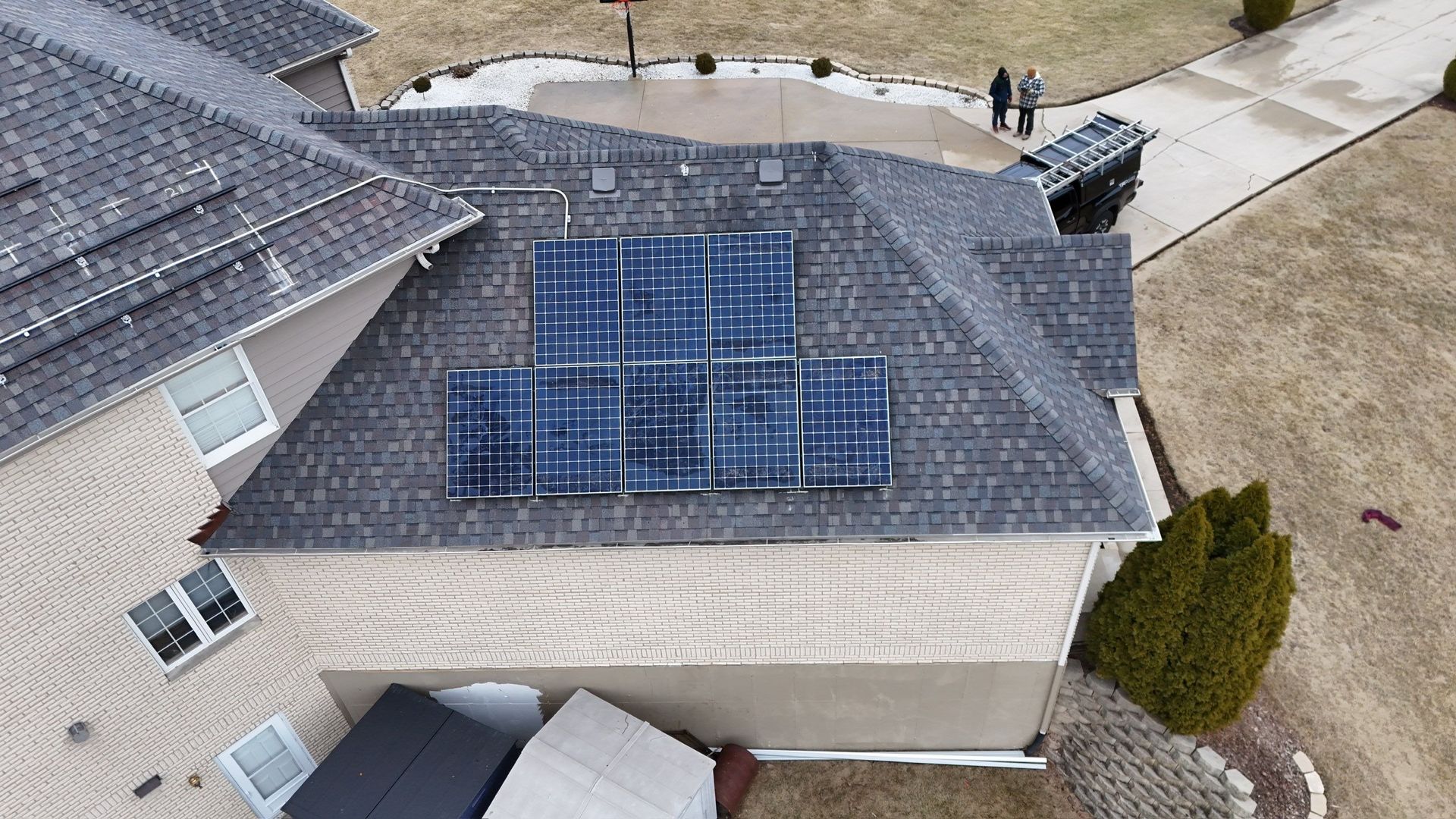An aerial view shows solar panels installed on a gray shingled rooftop of a house.