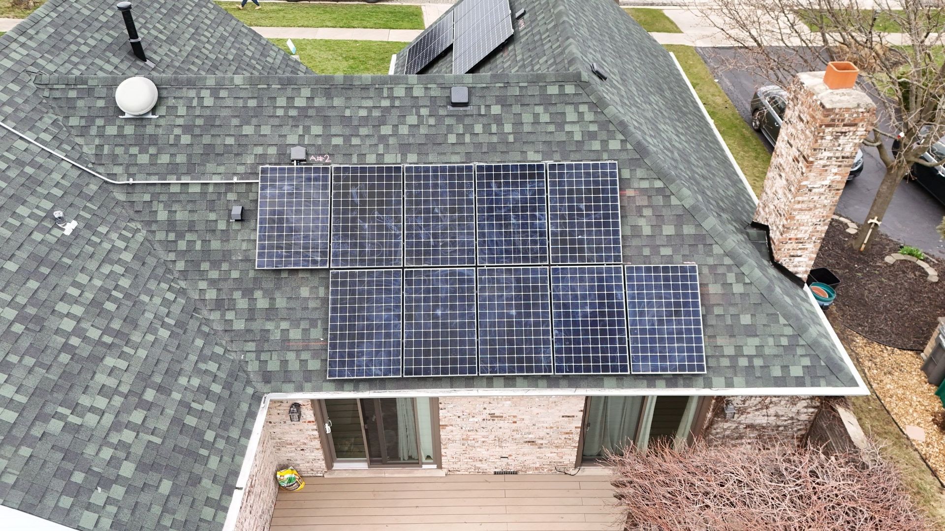Solar panels on a shingled roof of a house with a brick chimney.