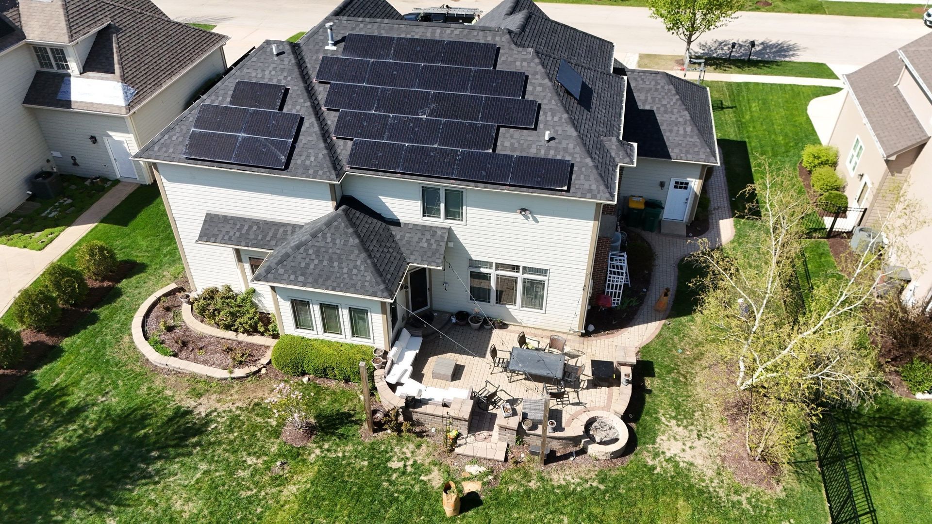 A two-story house with solar panels on the roof and a backyard patio with furniture.